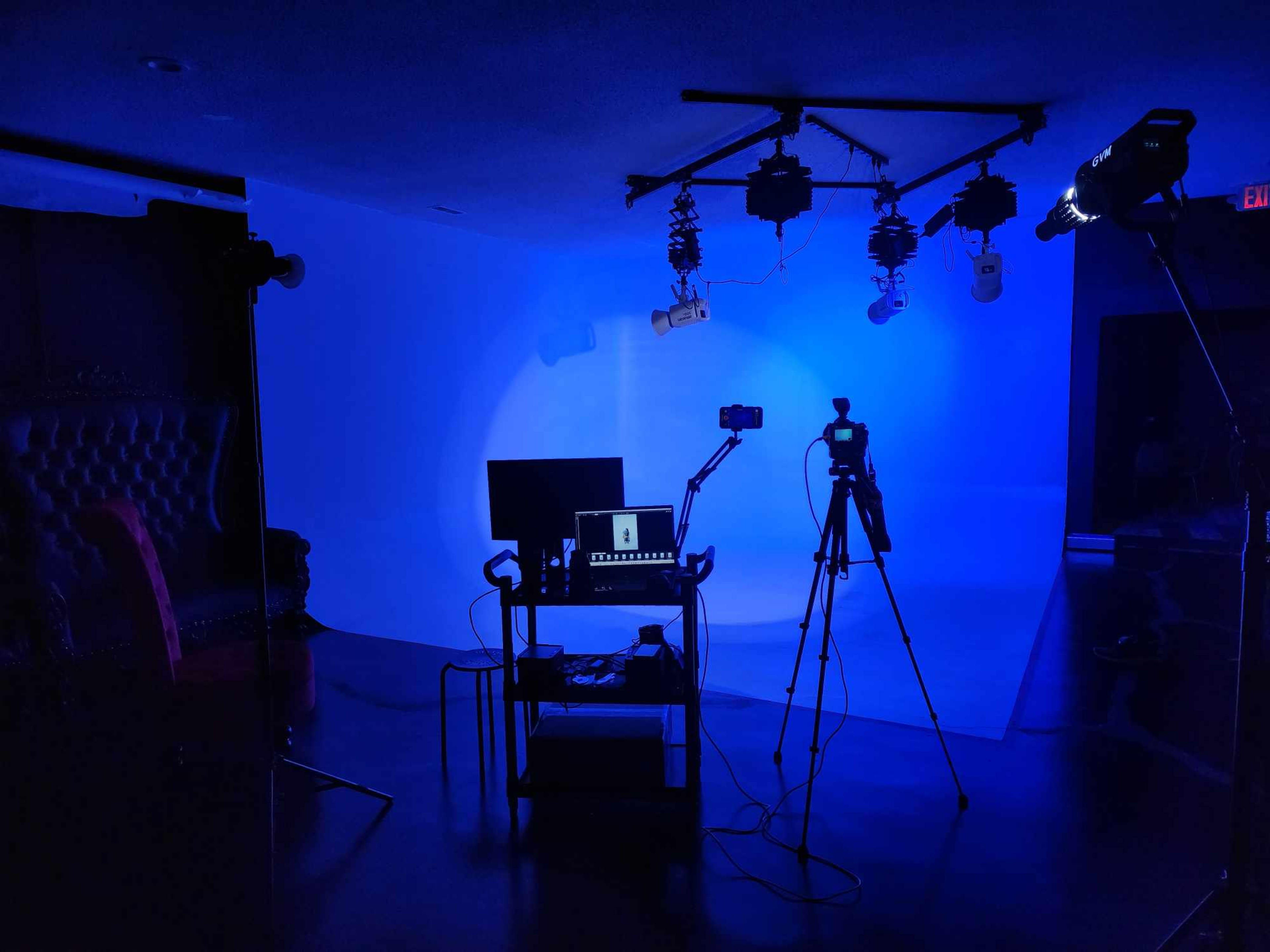 A dimly lit studio setup with a blue backdrop, a table with equipment, and two cameras on tripods.