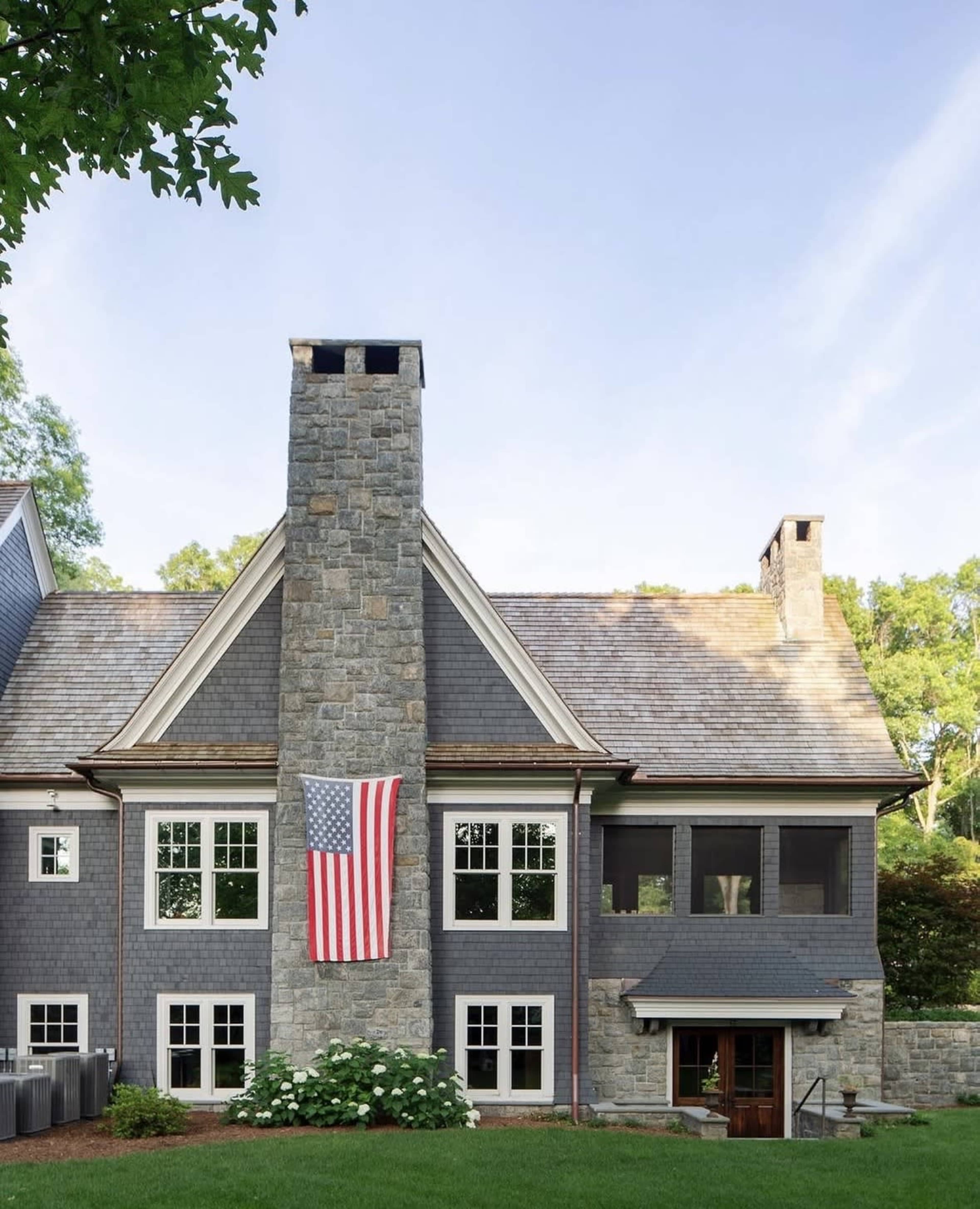 The image shows a large house with a prominent stone chimney and an American flag hanging on the exterior wall.