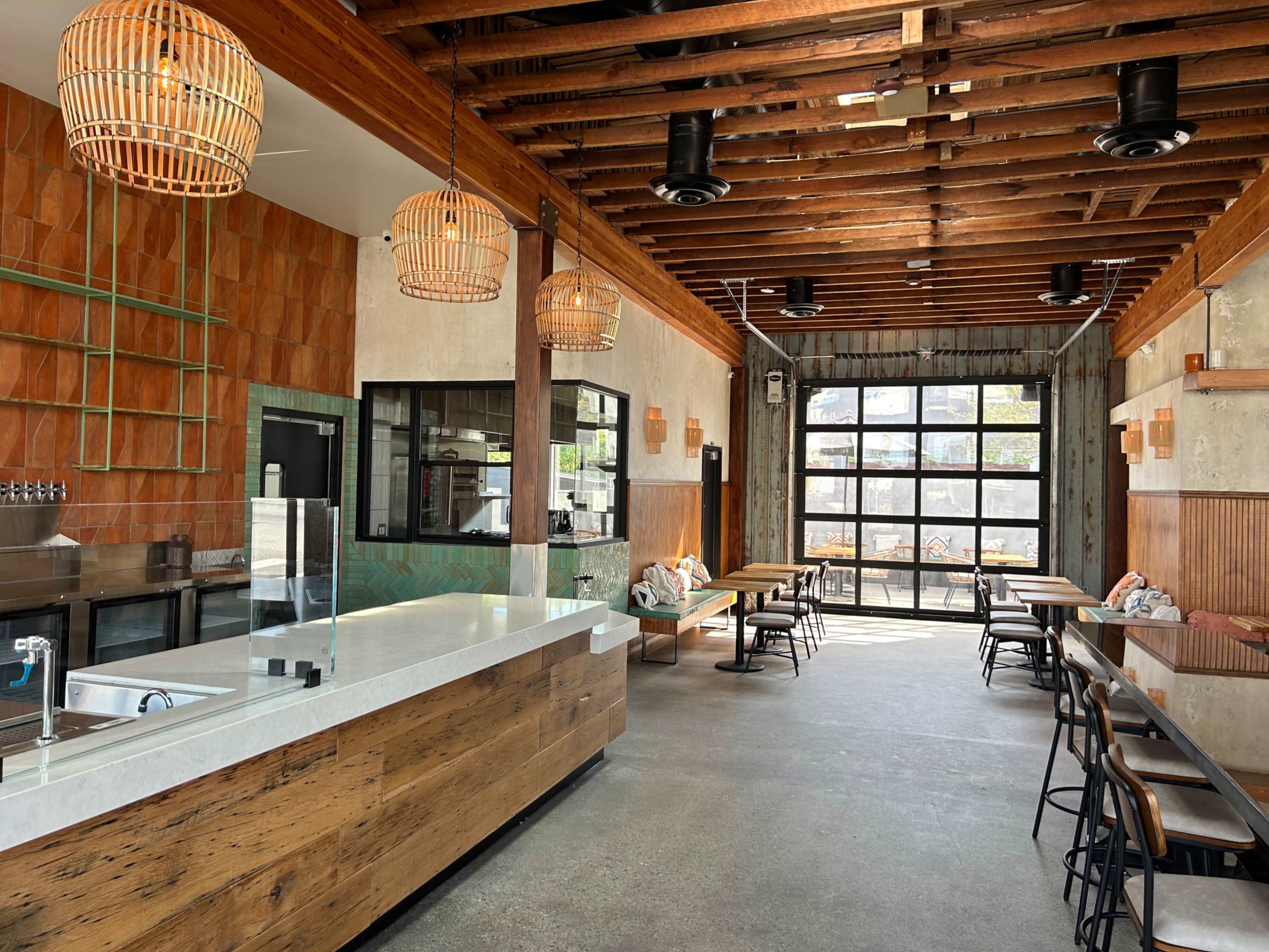 A modern café interior featuring a wooden counter, industrial-style décor, and large windows allowing natural light to enter.