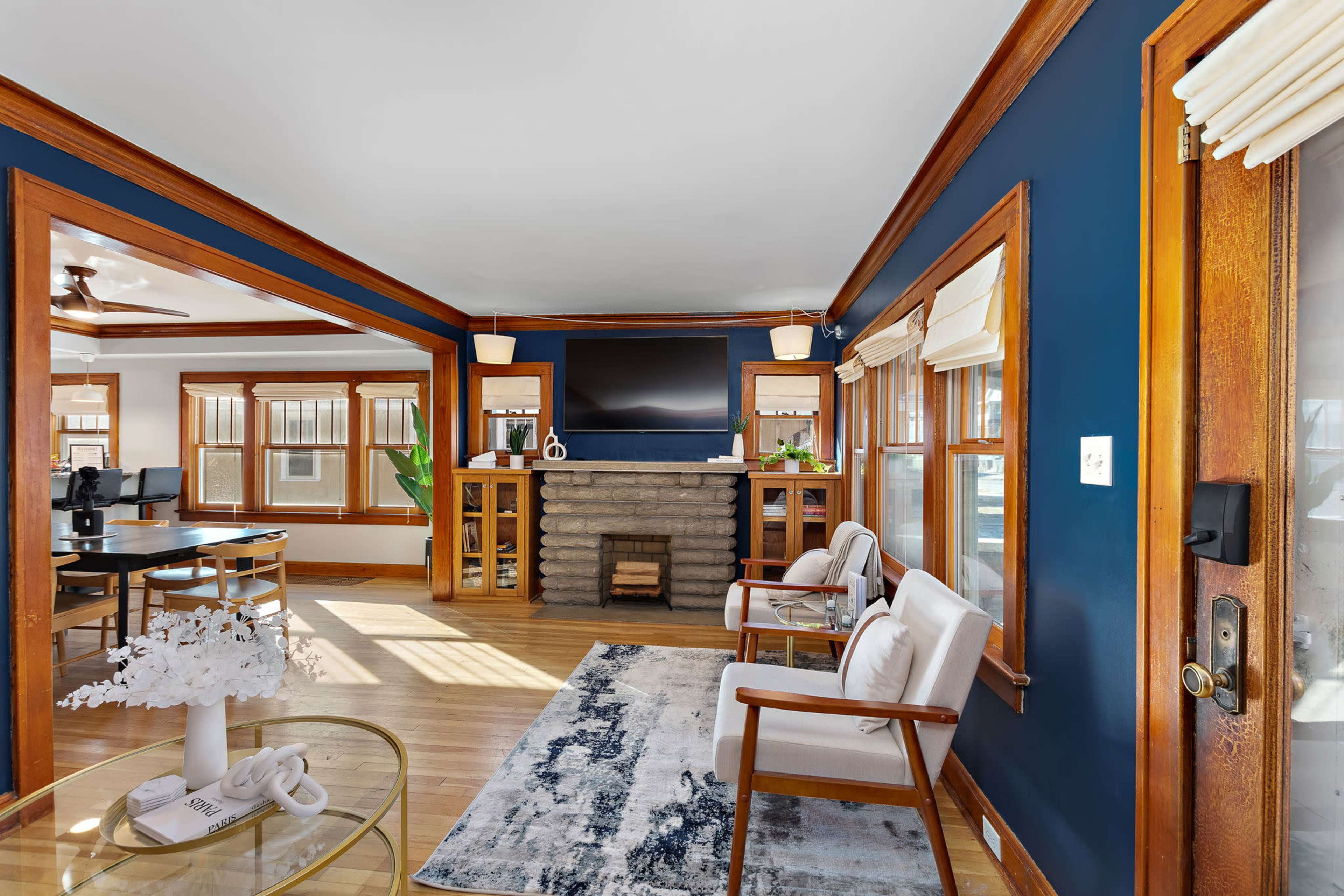 A room with dark blue walls, wooden trim, a stone fireplace, and two white armchairs arranged near a glass coffee table.