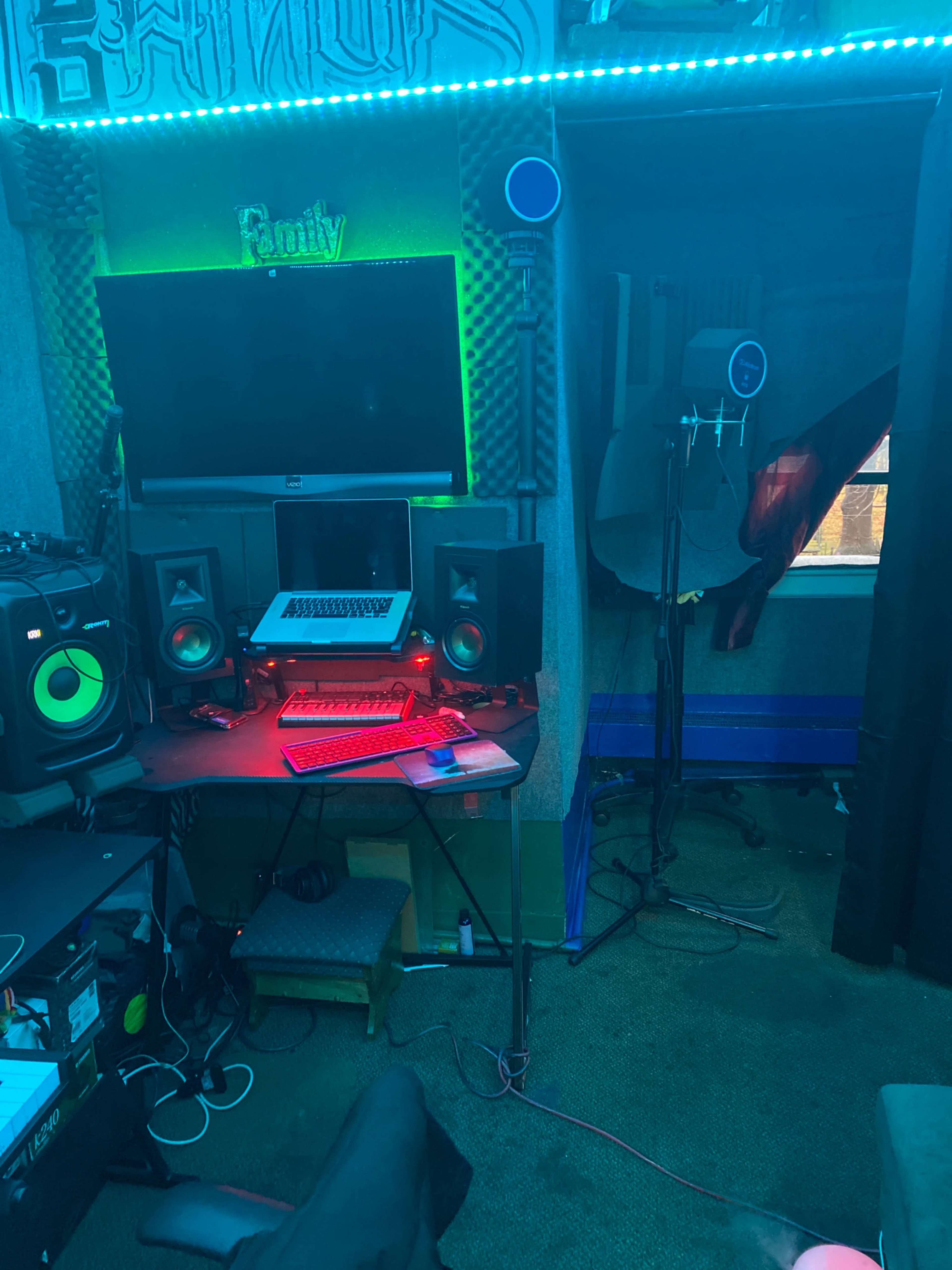 A music production setup in a small room with speakers, a computer, and various equipment against a backdrop of colorful lighting.