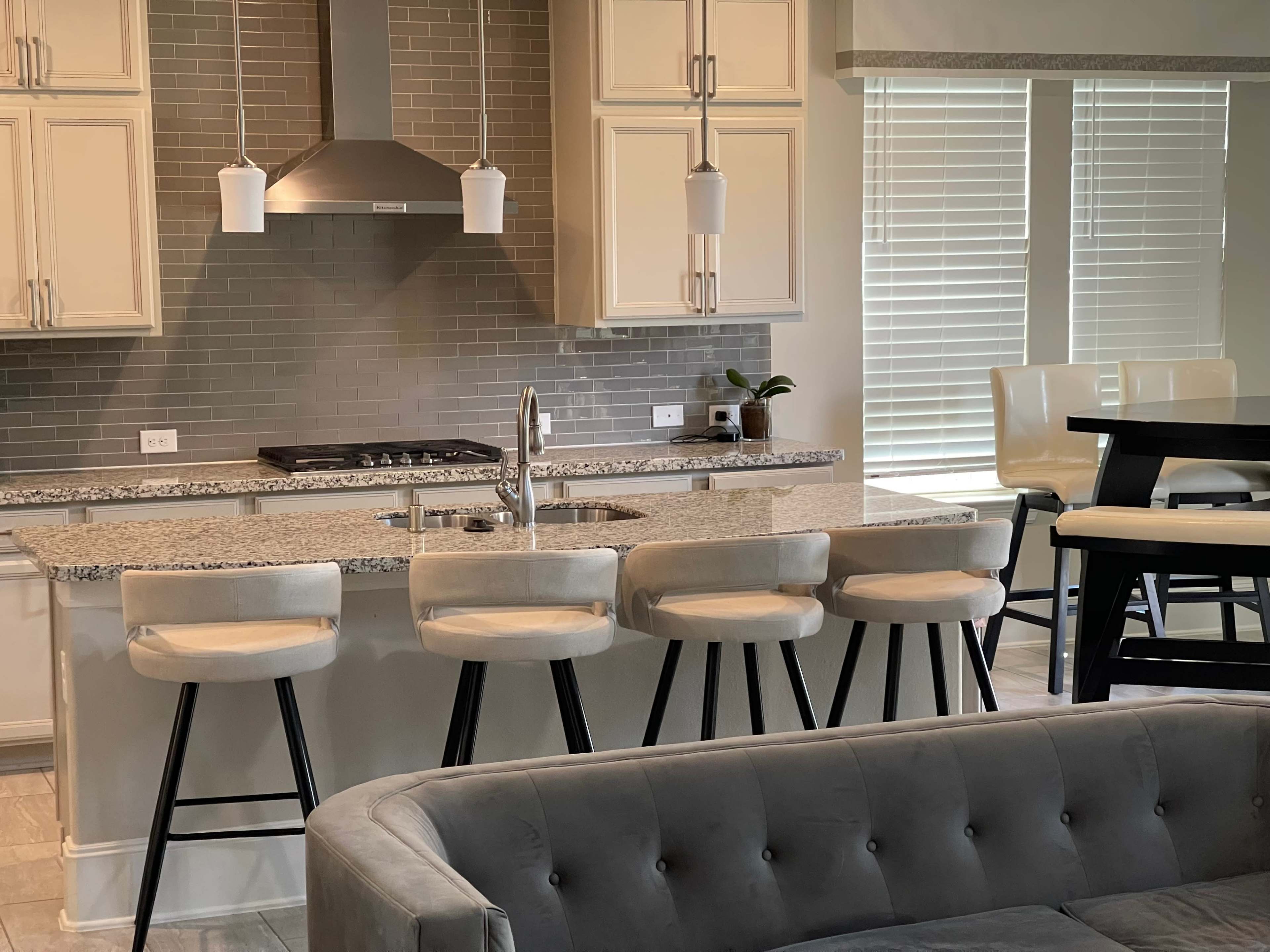 The image shows a modern kitchen with a granite countertop, bar seating, and a stainless steel range hood above the stove.