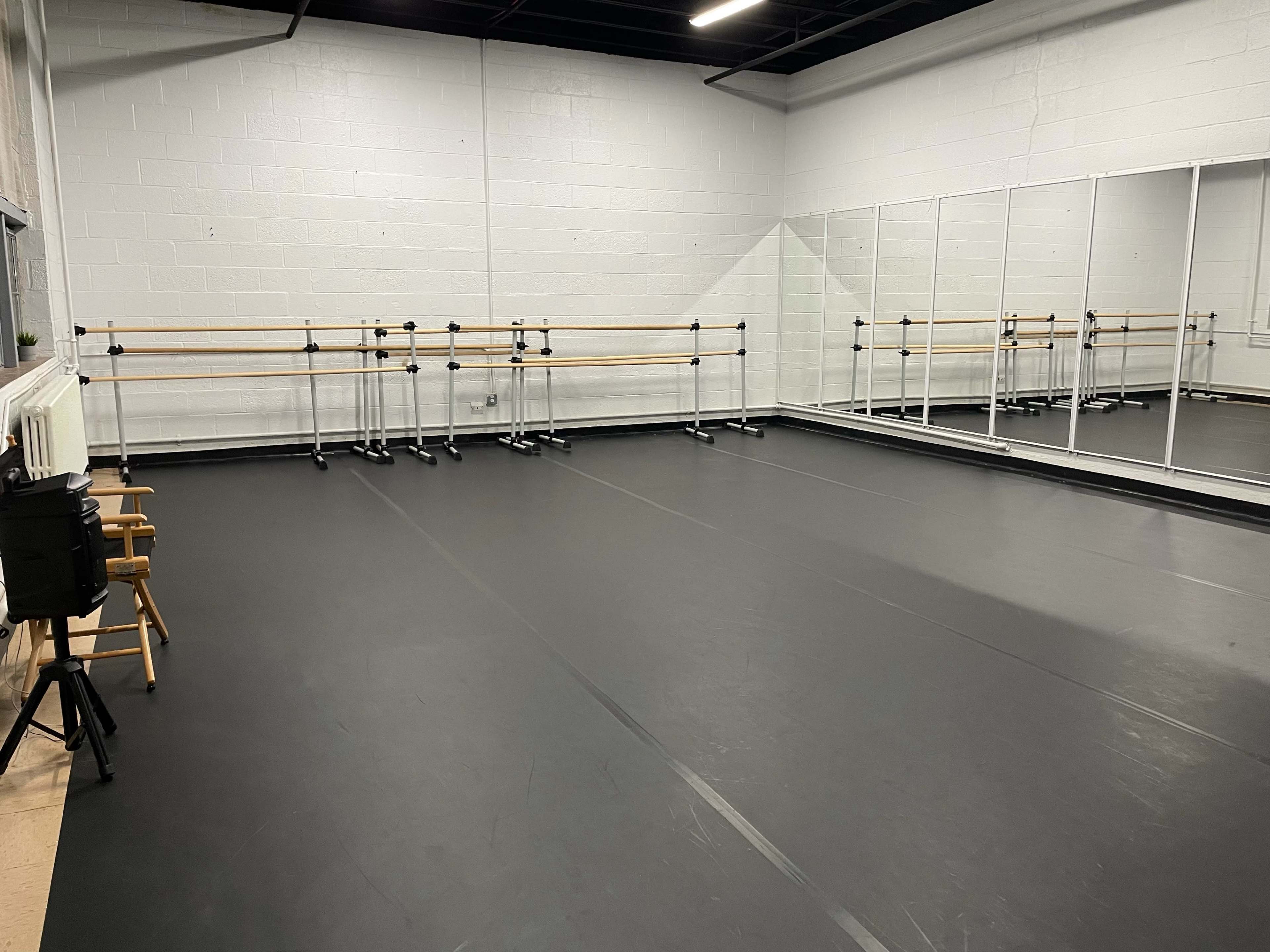 A spacious dance studio with black flooring, mirrored walls, and ballet bars along one side.