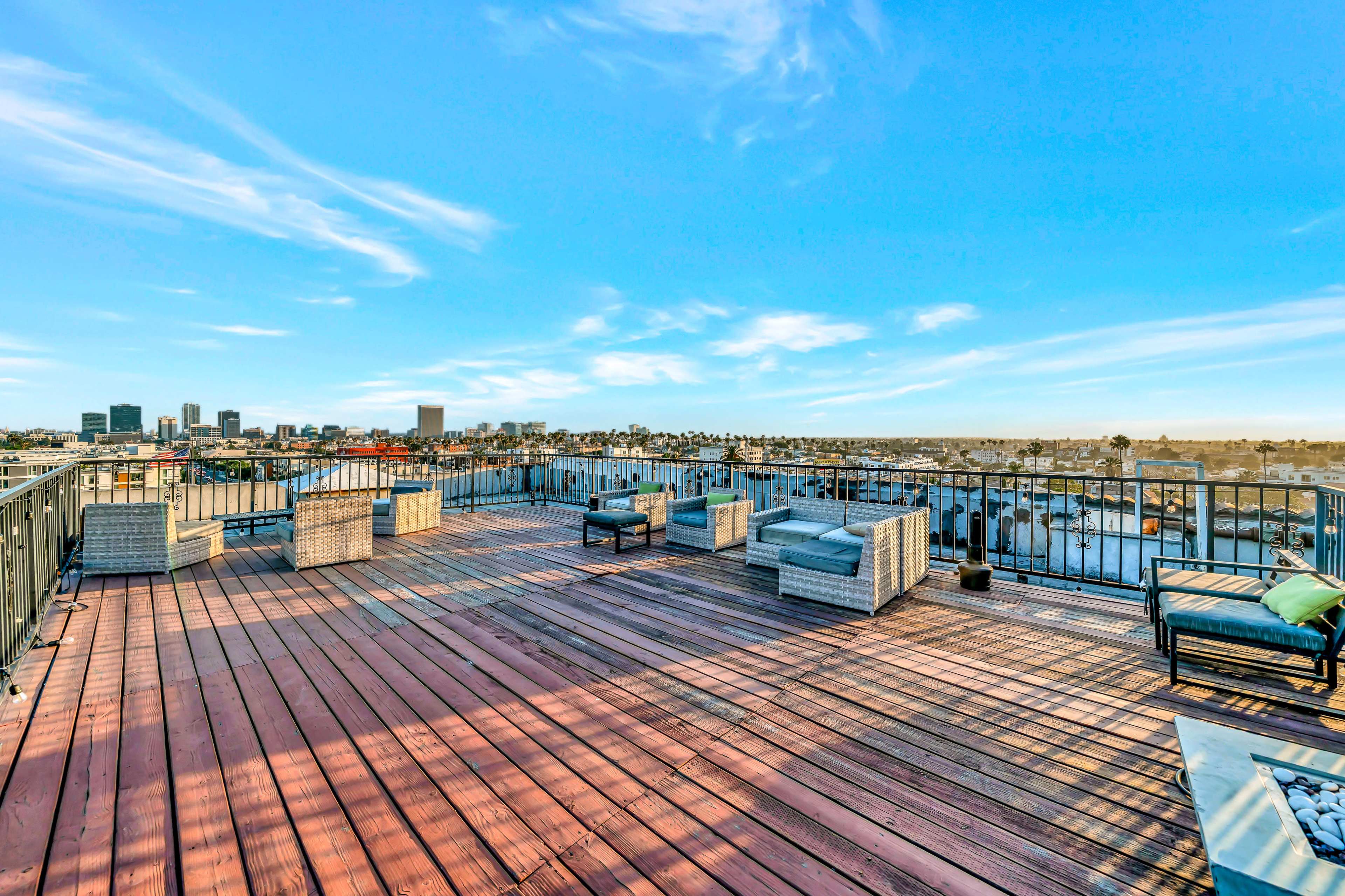 The image shows a spacious rooftop terrace with outdoor furniture and a panoramic view of the city skyline.