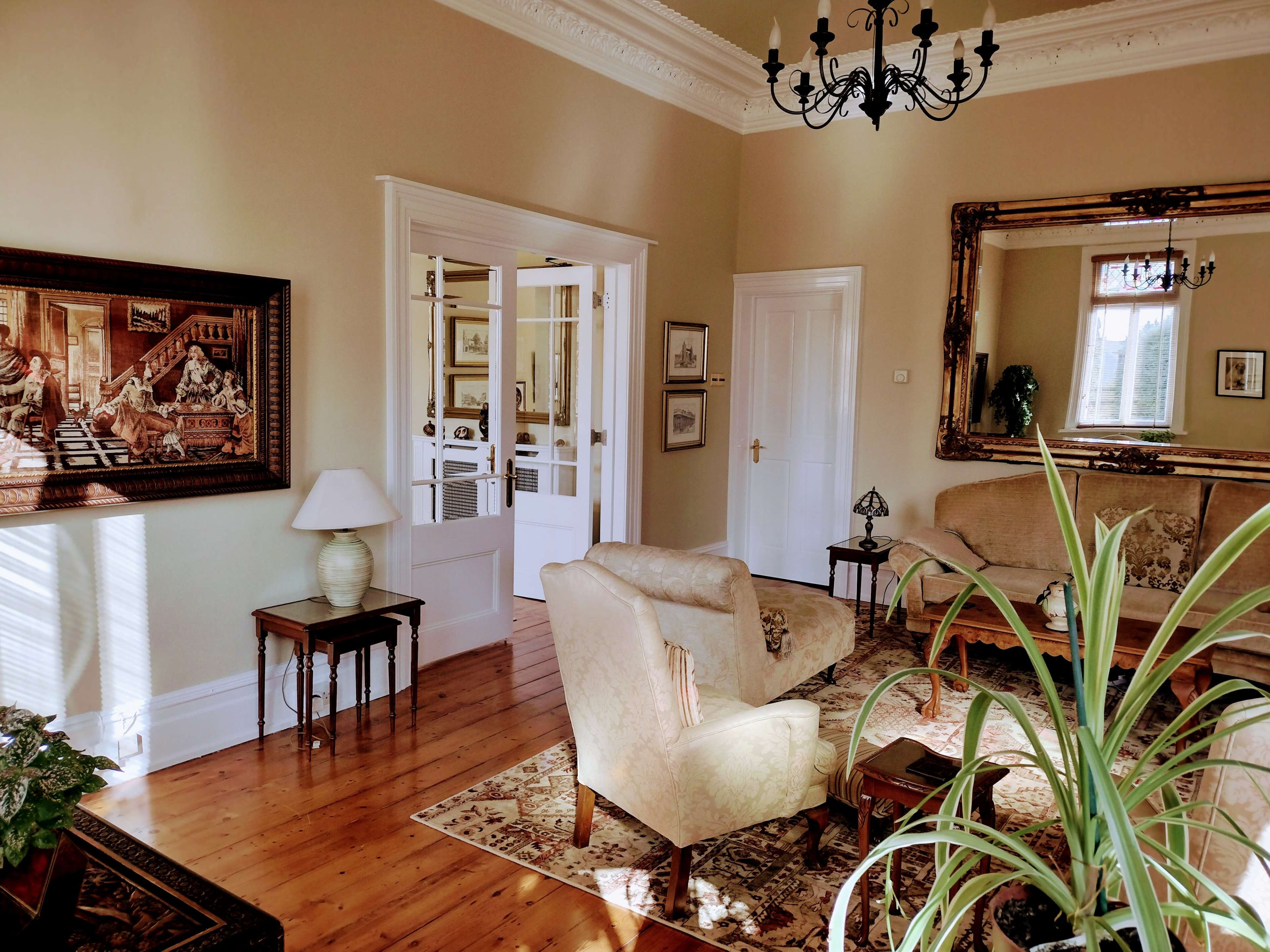 A well-furnished living room with a chandelier, a large mirror, and seating arranged around a central area.