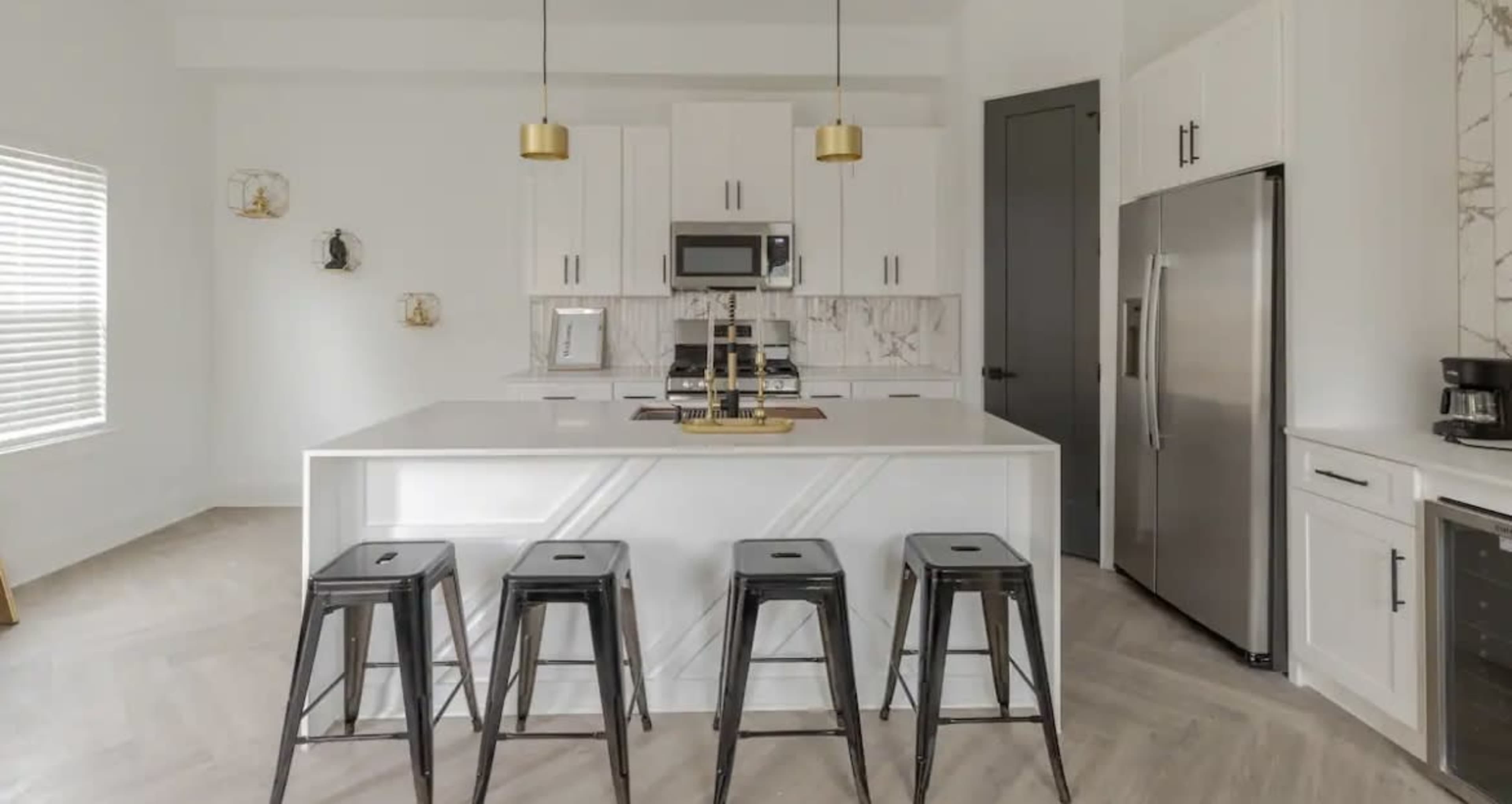 A modern kitchen features white cabinetry, stainless steel appliances, and a large island with metal stools.