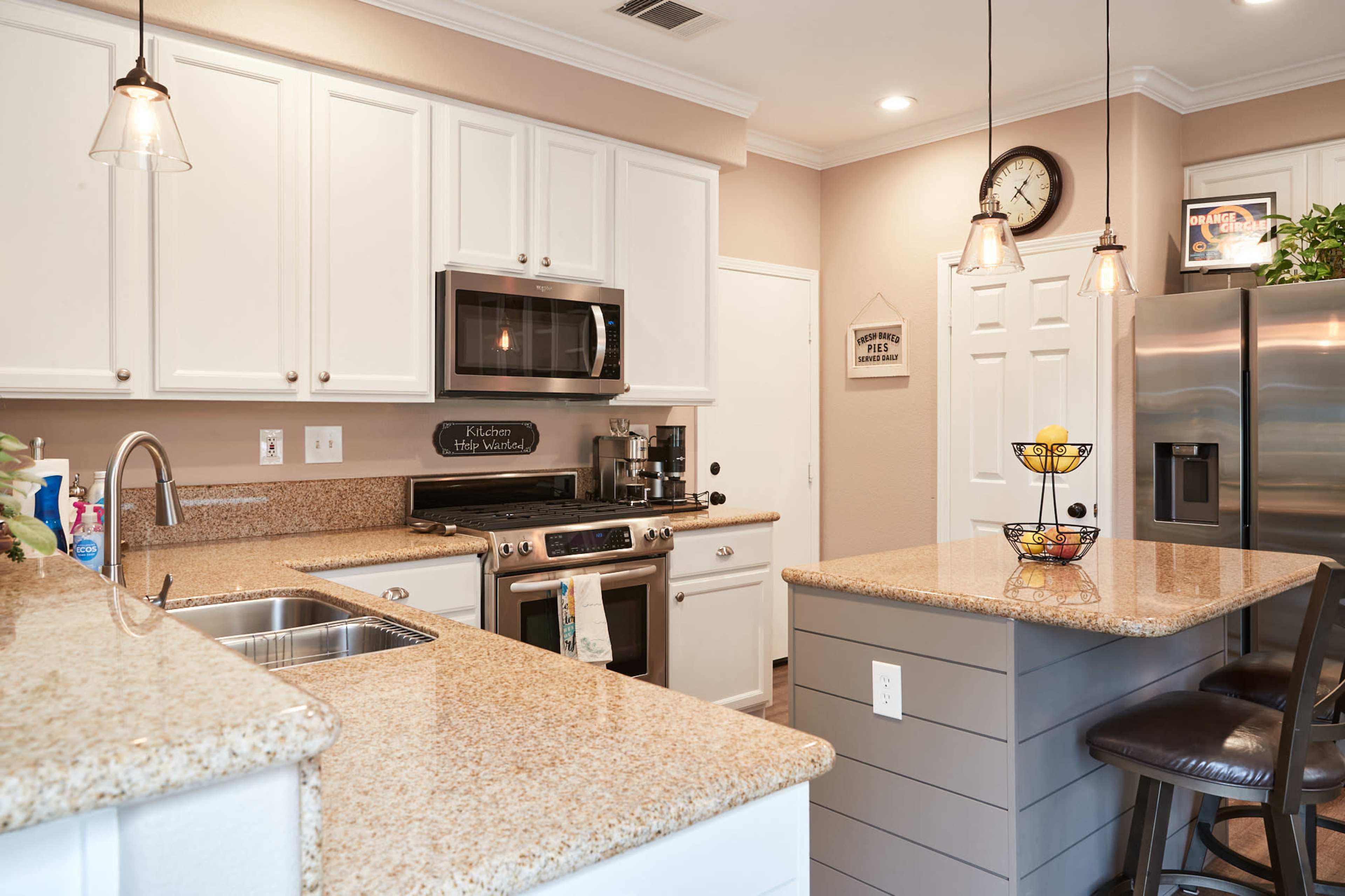 The kitchen features white cabinetry, a stainless steel refrigerator, a microwave built into the wall, and a central island with a granite countertop.
