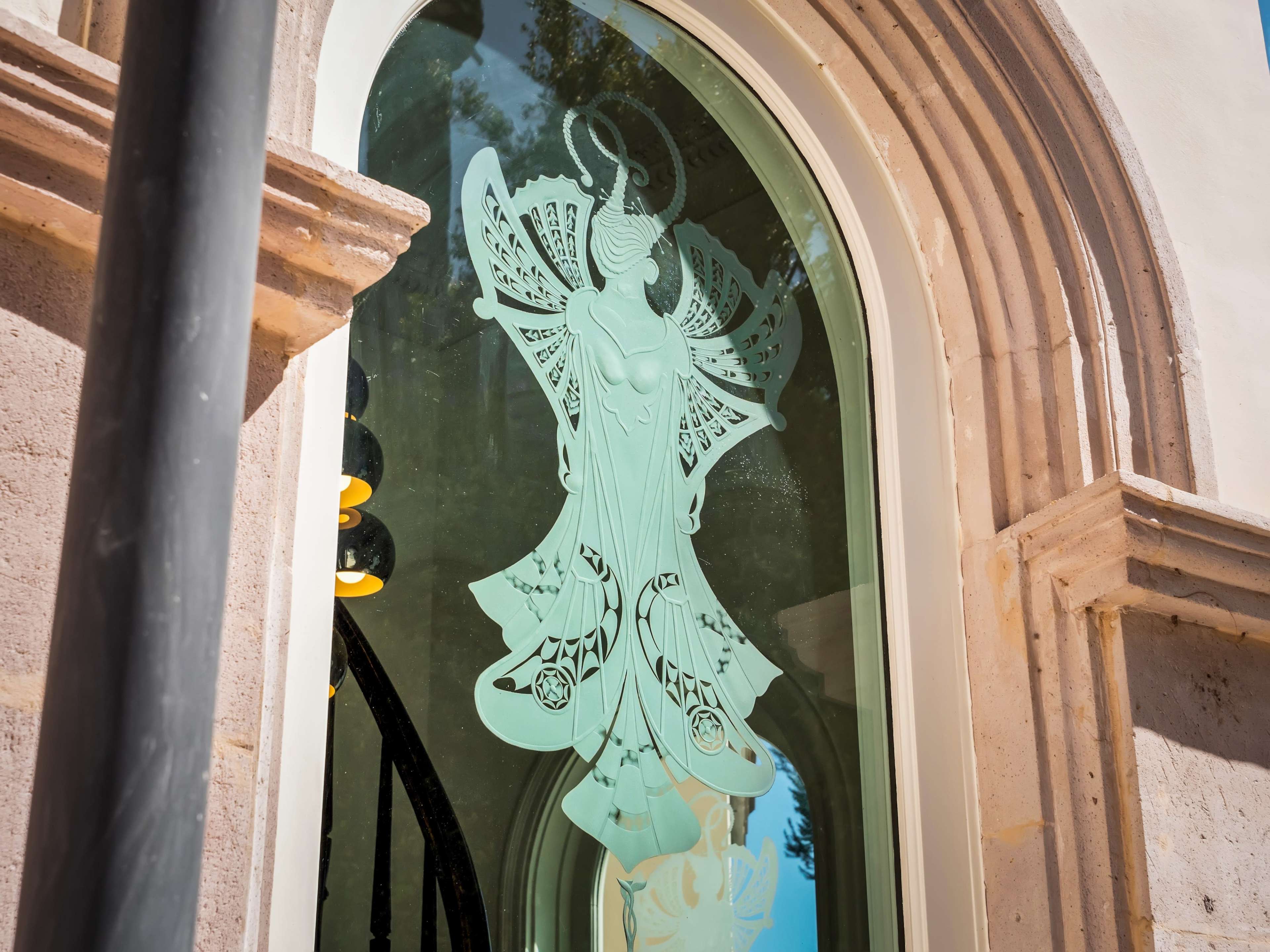 A decorative glass window features an intricate design of a figure with elaborate wings and flowing garments.