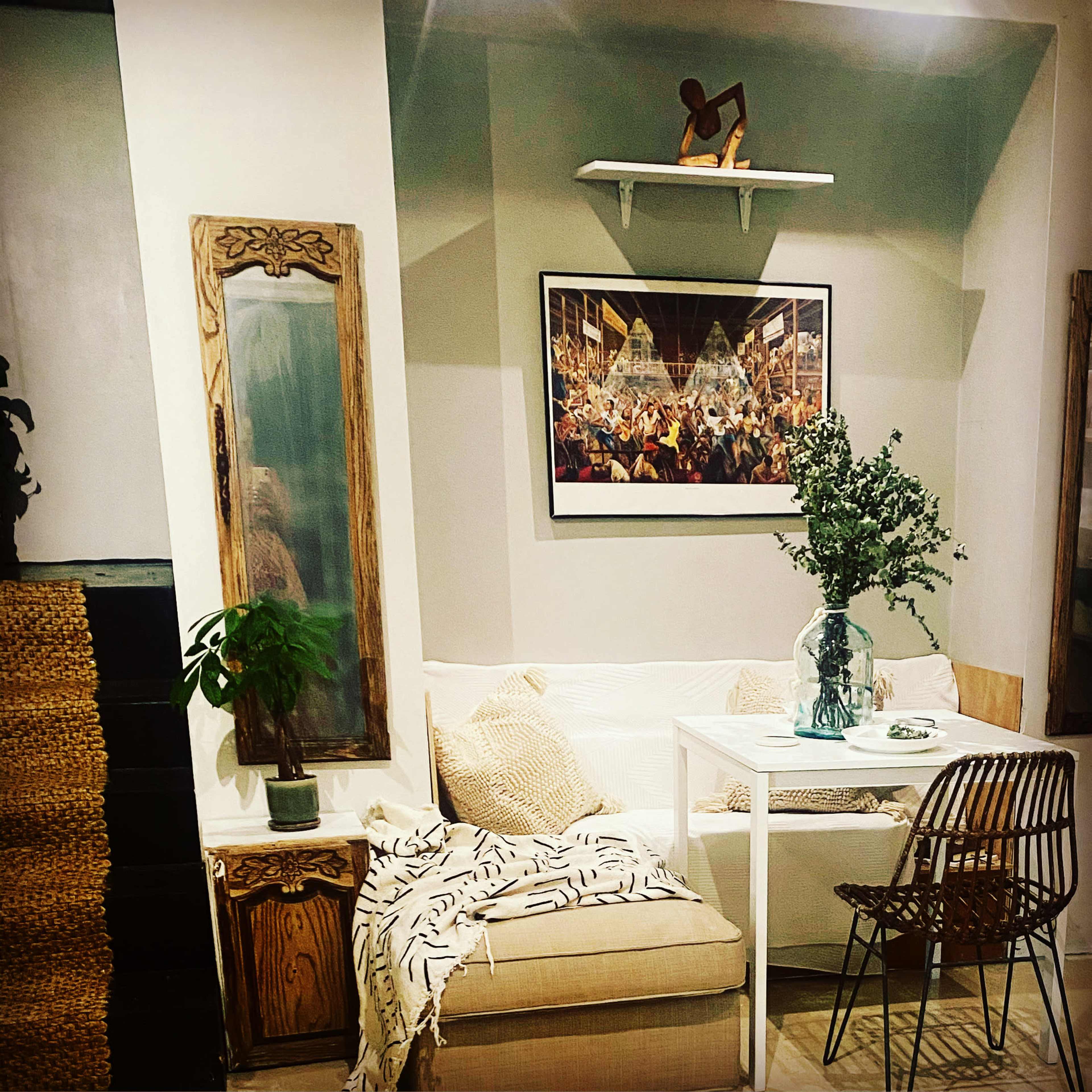 A cozy corner of a living space featuring a sofa, a table with a vase of flowers, and a piece of wall art above a shelf.