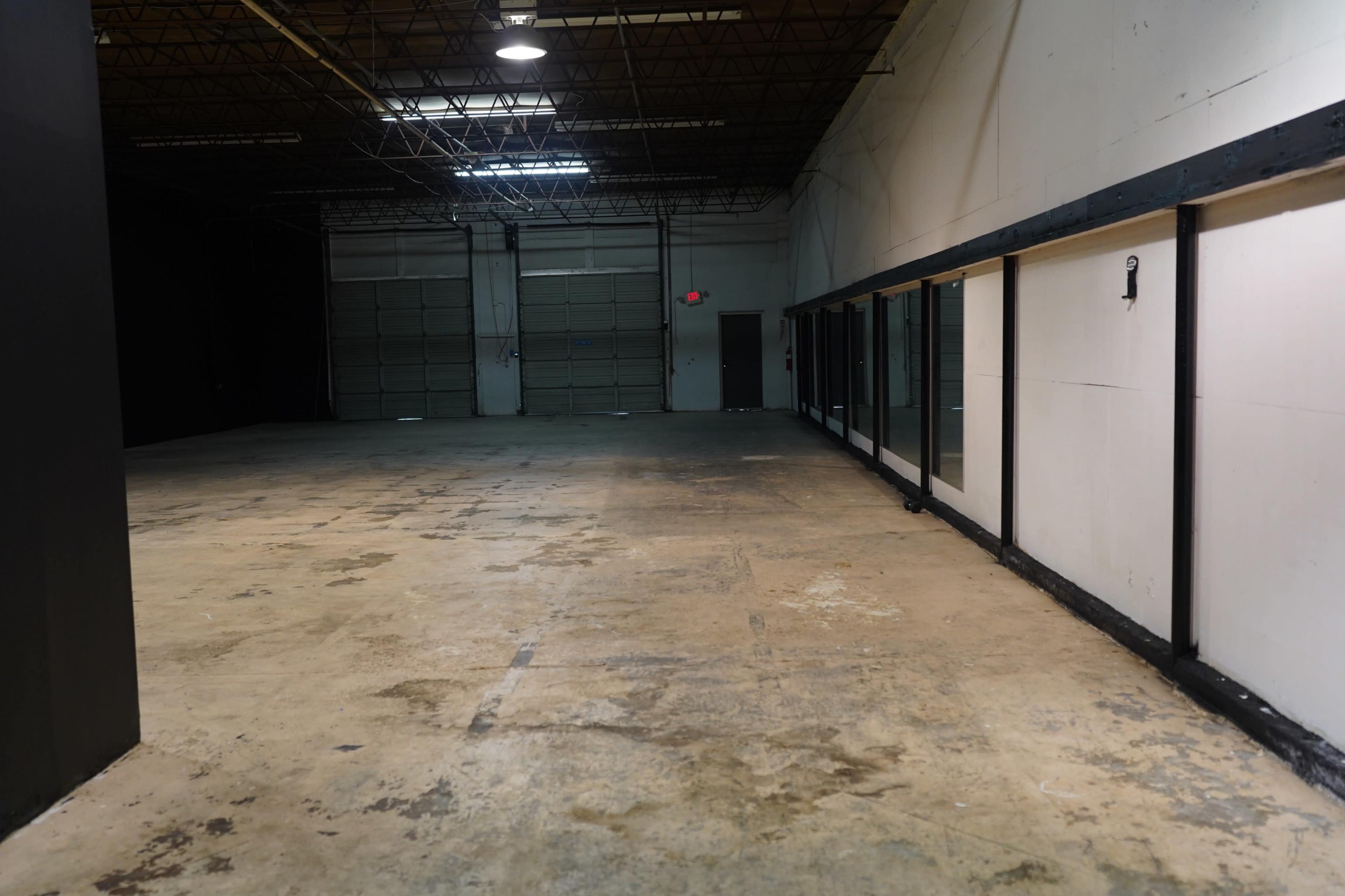 The image shows a spacious, empty warehouse interior with a concrete floor and large, closed garage doors at one end.