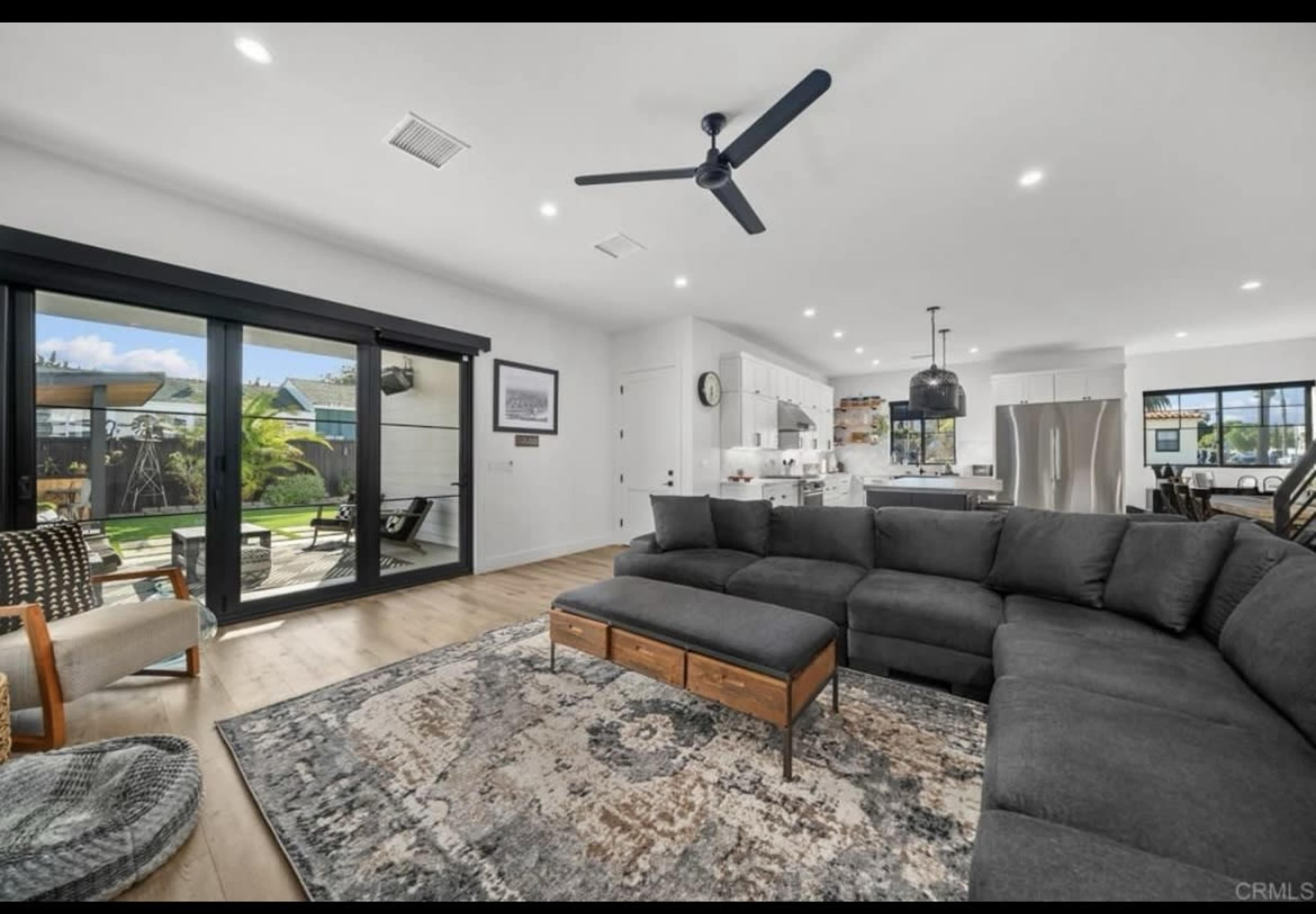 The image shows a modern living room with a large sectional sofa, a patterned area rug, and open access to an outdoor area through glass sliding doors.