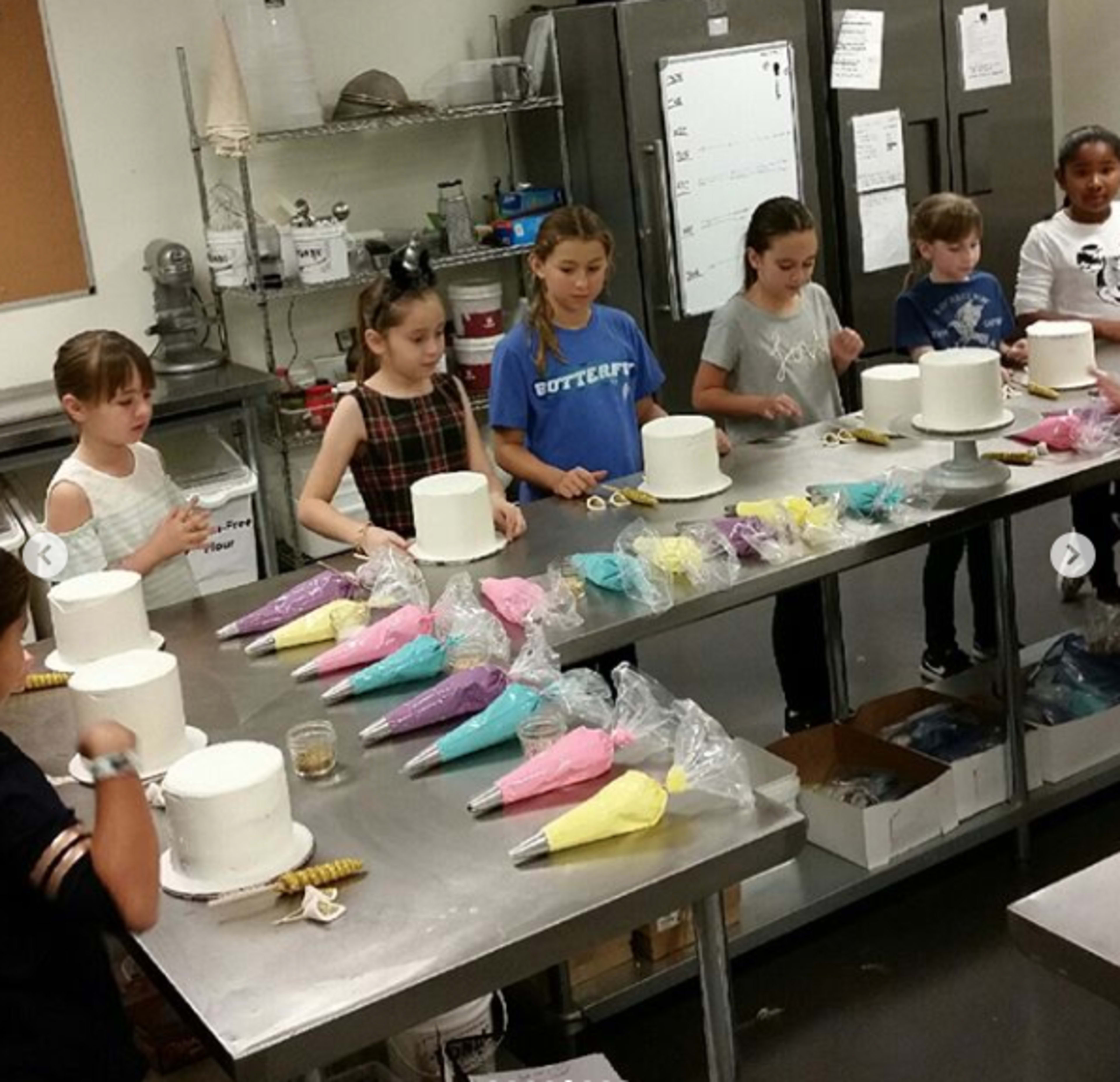 A group of children is decorating white cakes with colorful icing in a kitchen setting.