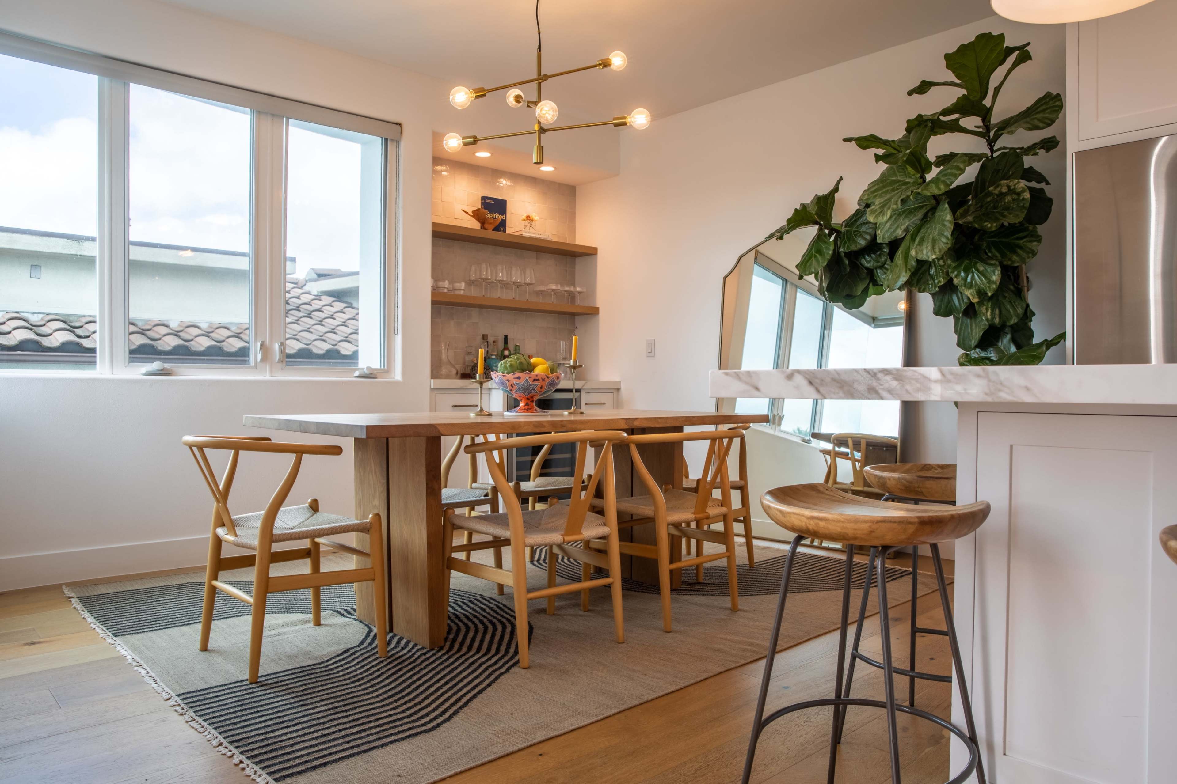 A modern dining area featuring a wooden table surrounded by chairs, with a large window and a patterned rug on the floor.