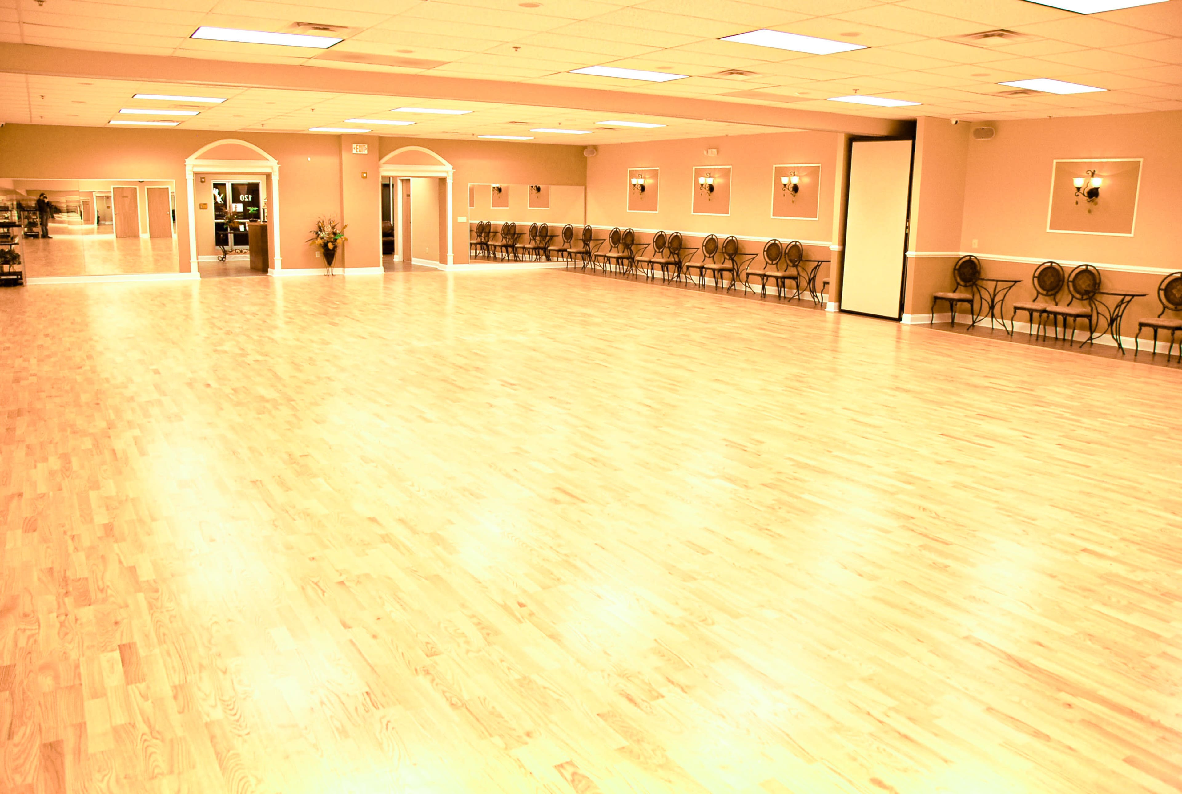 A spacious dance studio with polished wooden floors and a line of chairs against the back wall.