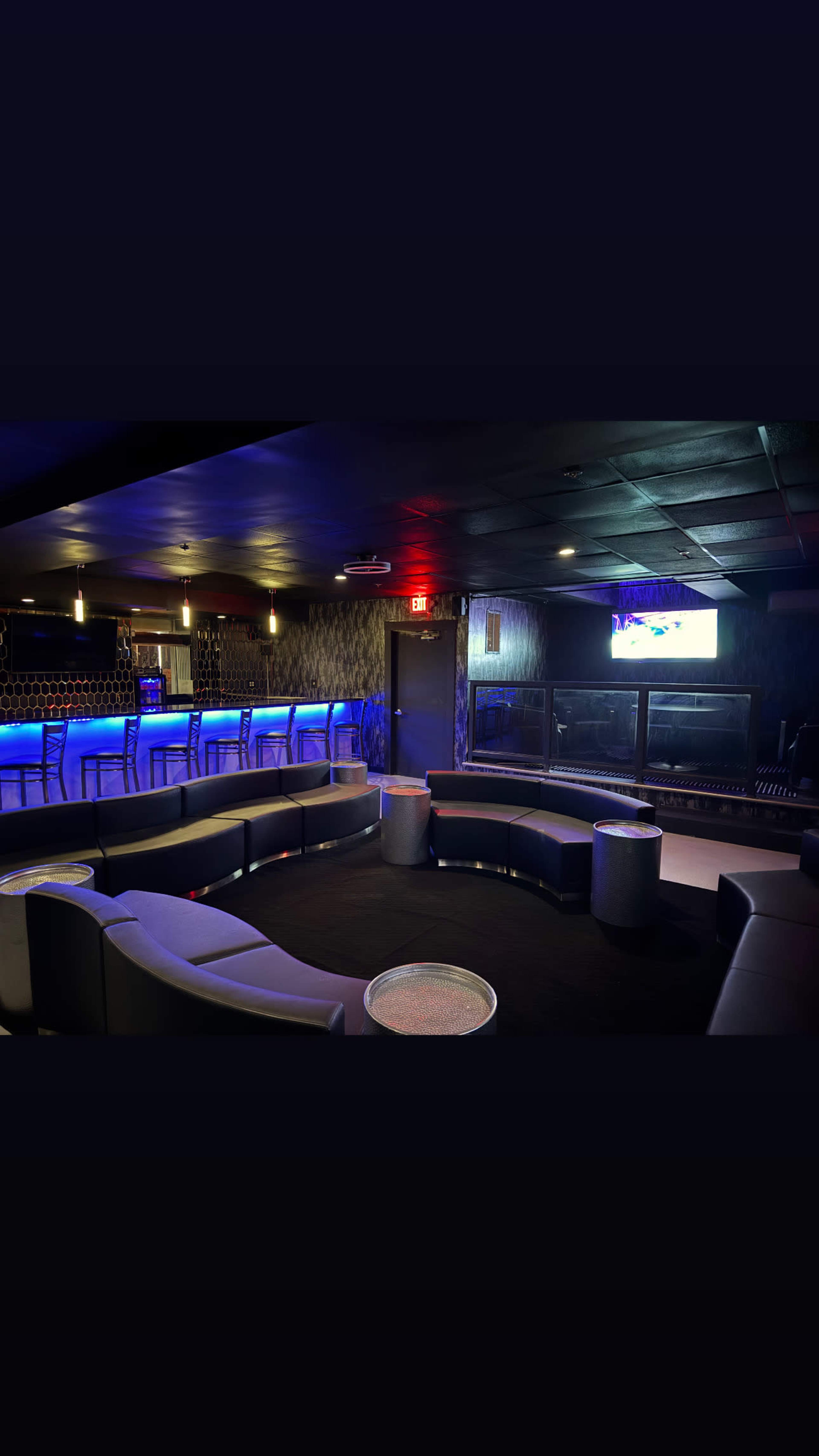The image shows a stylish lounge with blue ambient lighting, curved seating, and a bar area featuring high chairs.