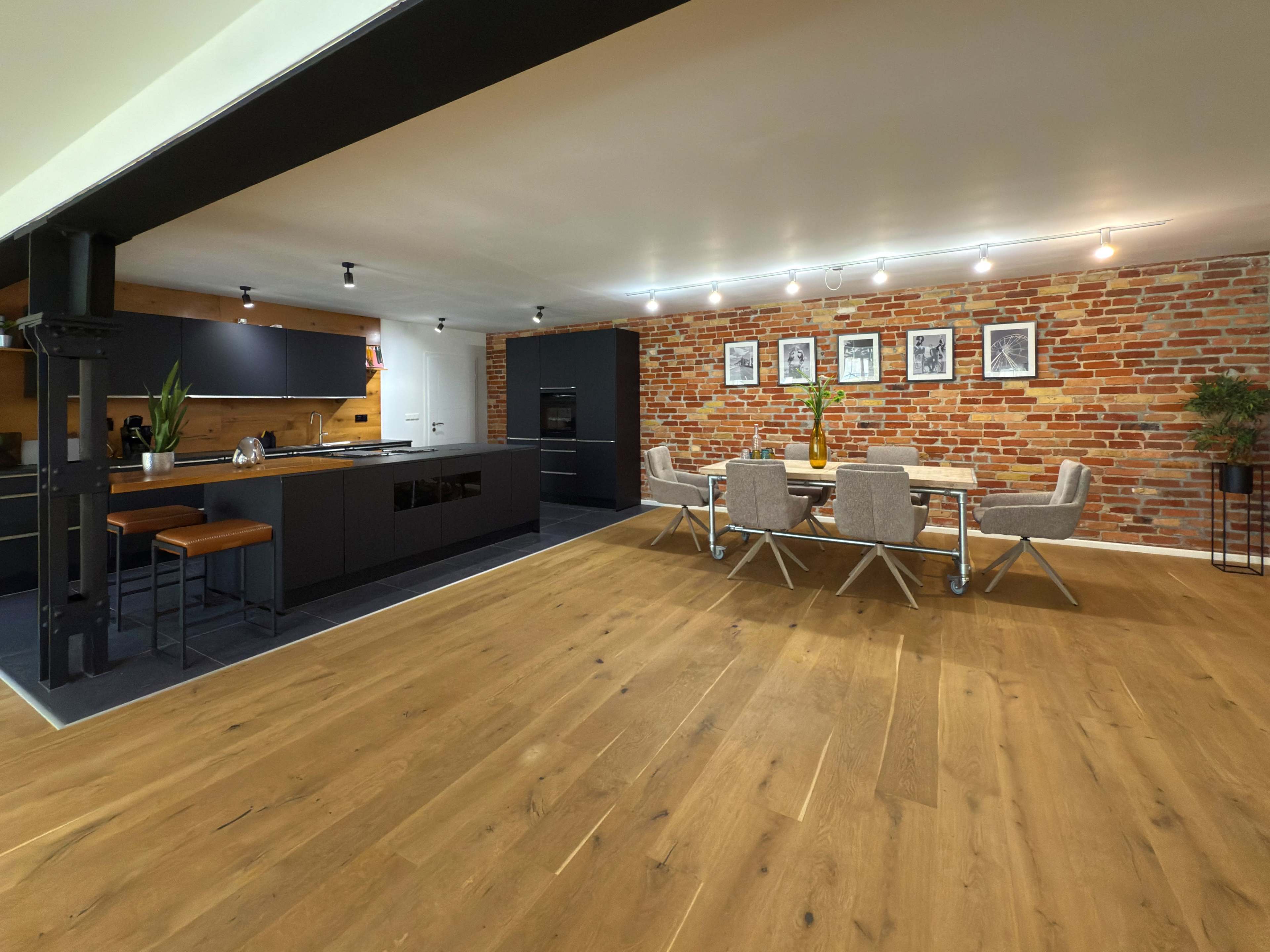 The image depicts a modern kitchen and dining area with a brick wall, wooden floor, and contemporary furniture.