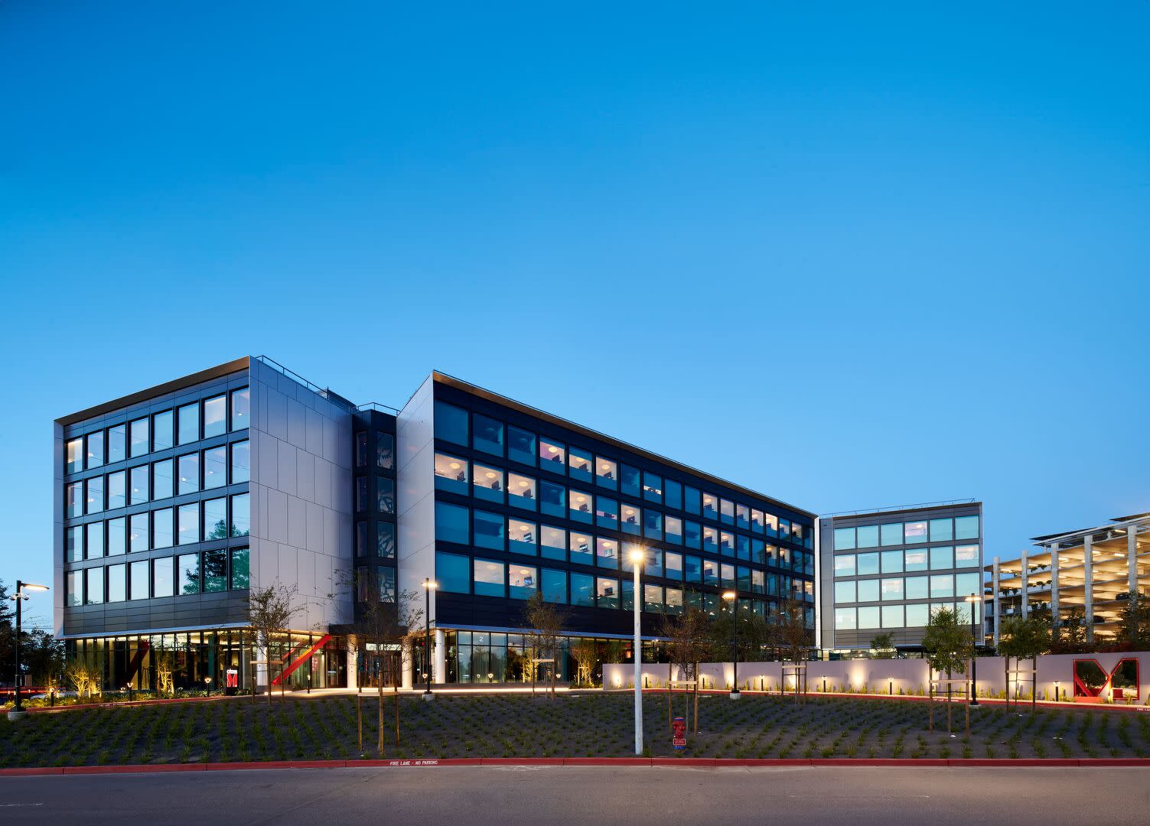 A modern office building with large glass windows and a landscaped area in the foreground, set against a clear blue sky.