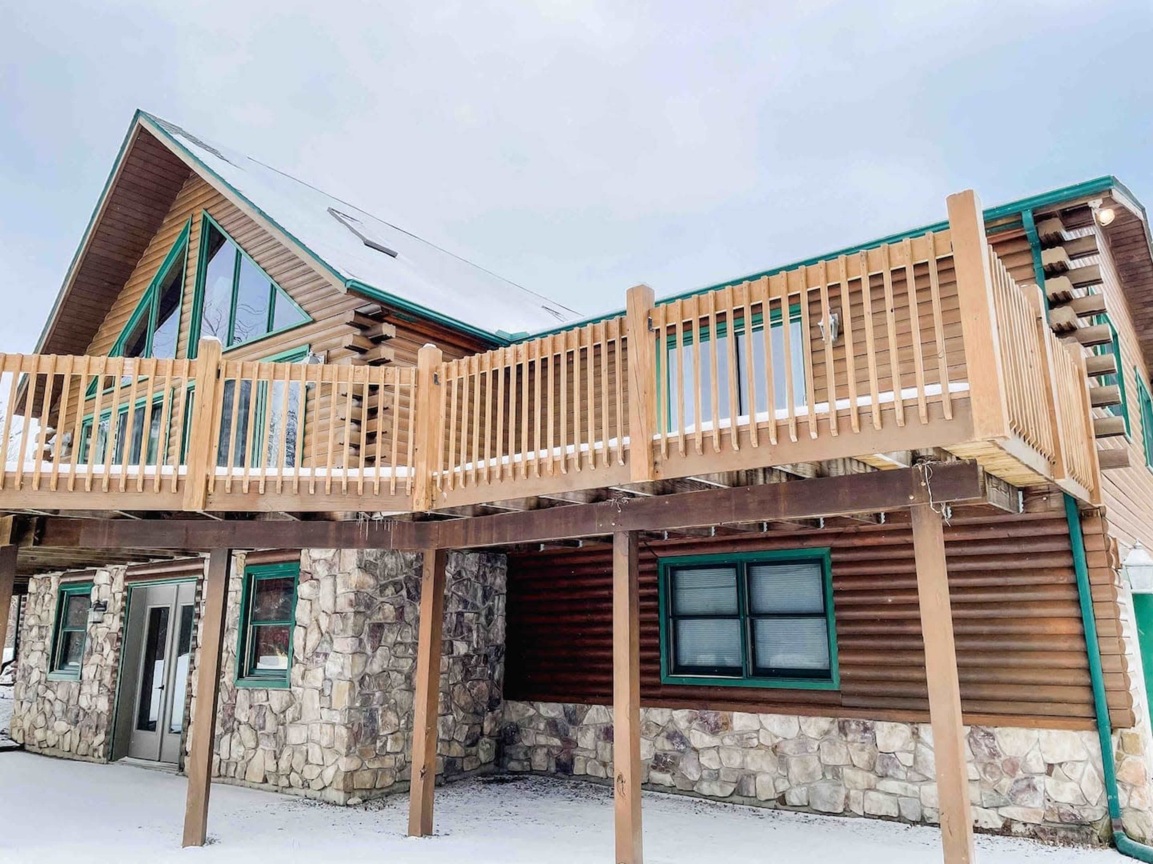 A two-story wooden cabin with a stone foundation and a large wooden deck on the upper level.