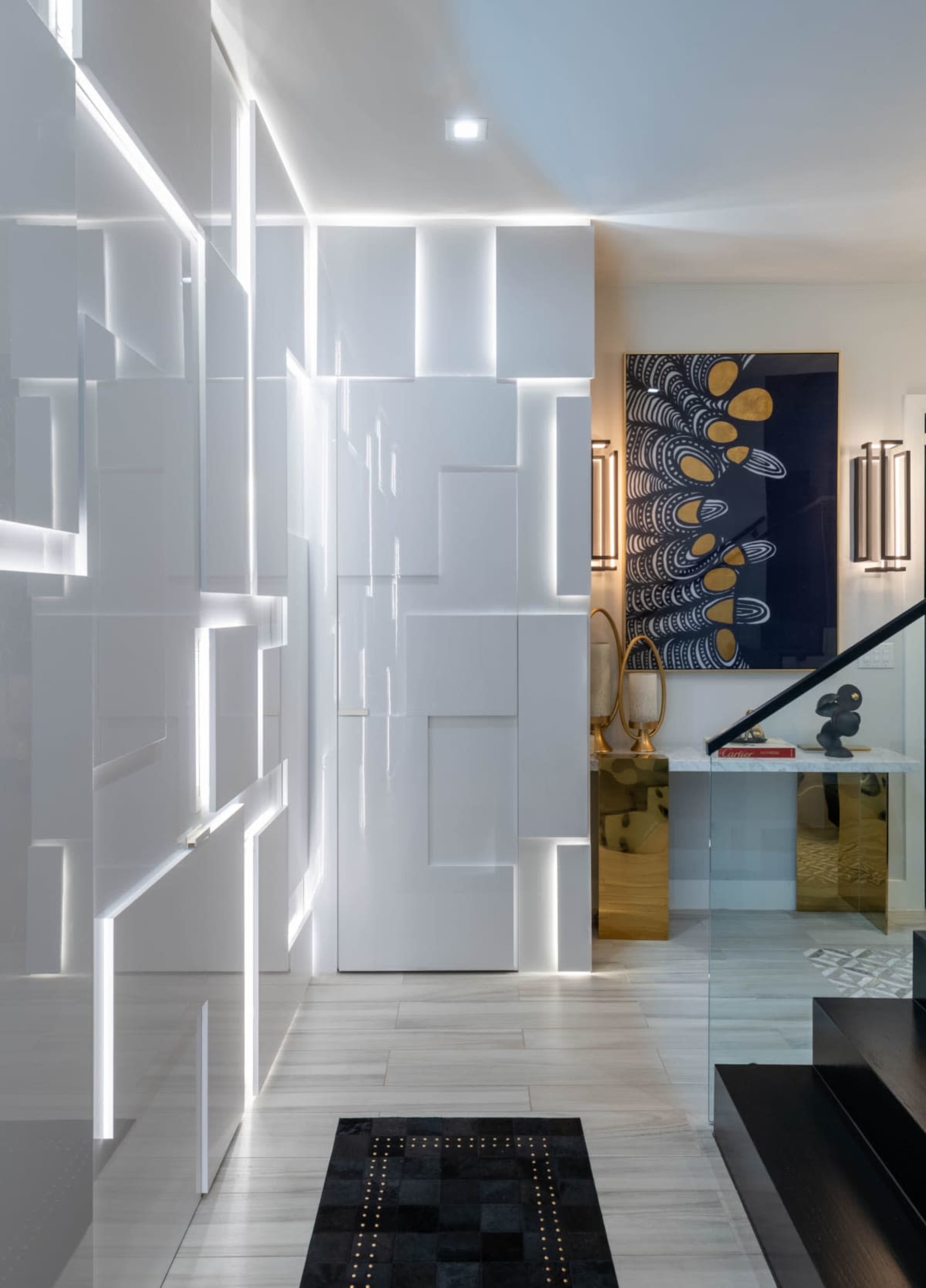 The image shows a modern hallway with geometric white panels illuminated by LED lights, leading towards a staircase and a decorative wall hanging.