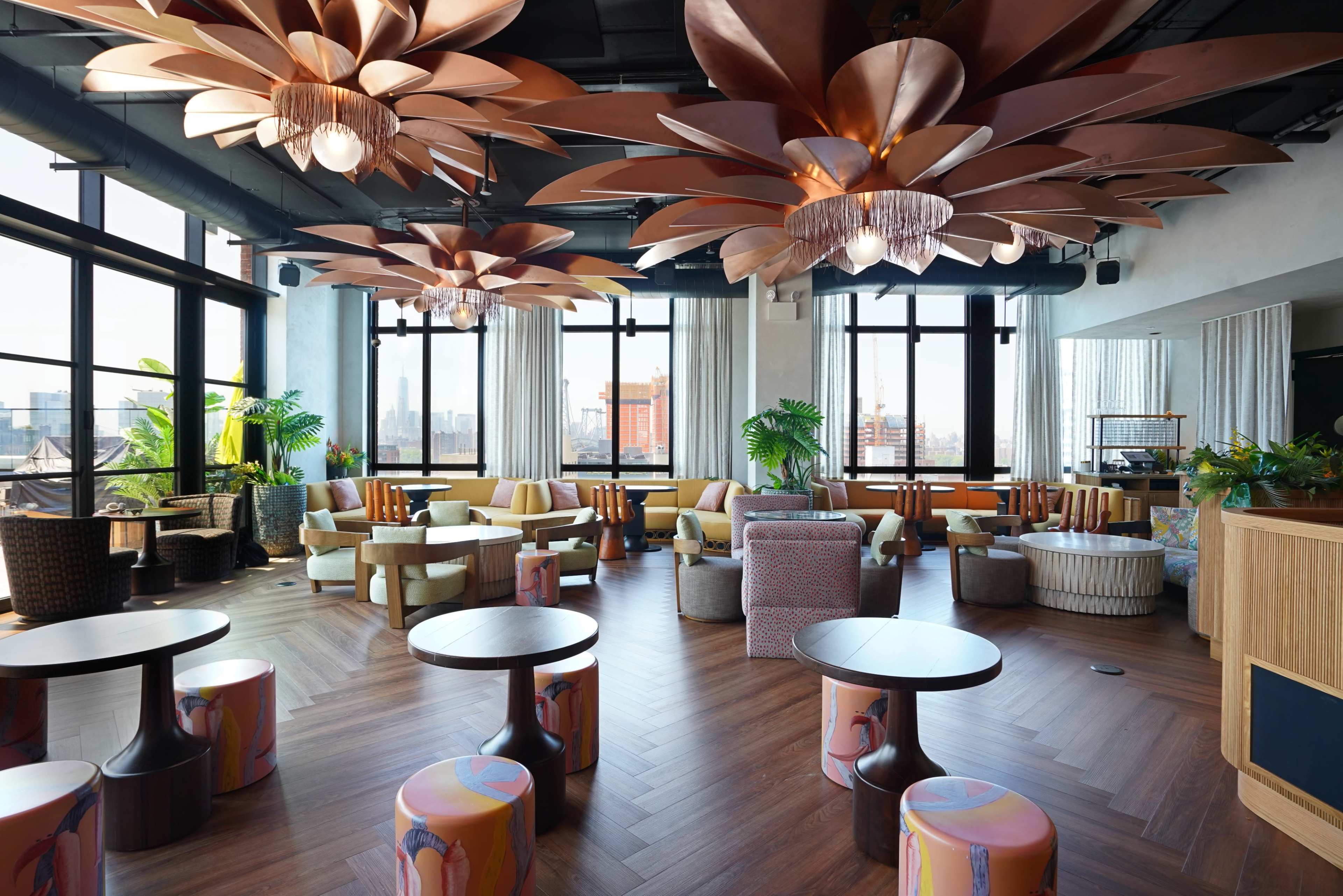 The image shows a bright, modern lounge with large windows, featuring unique floral ceiling fixtures and various seating arrangements.