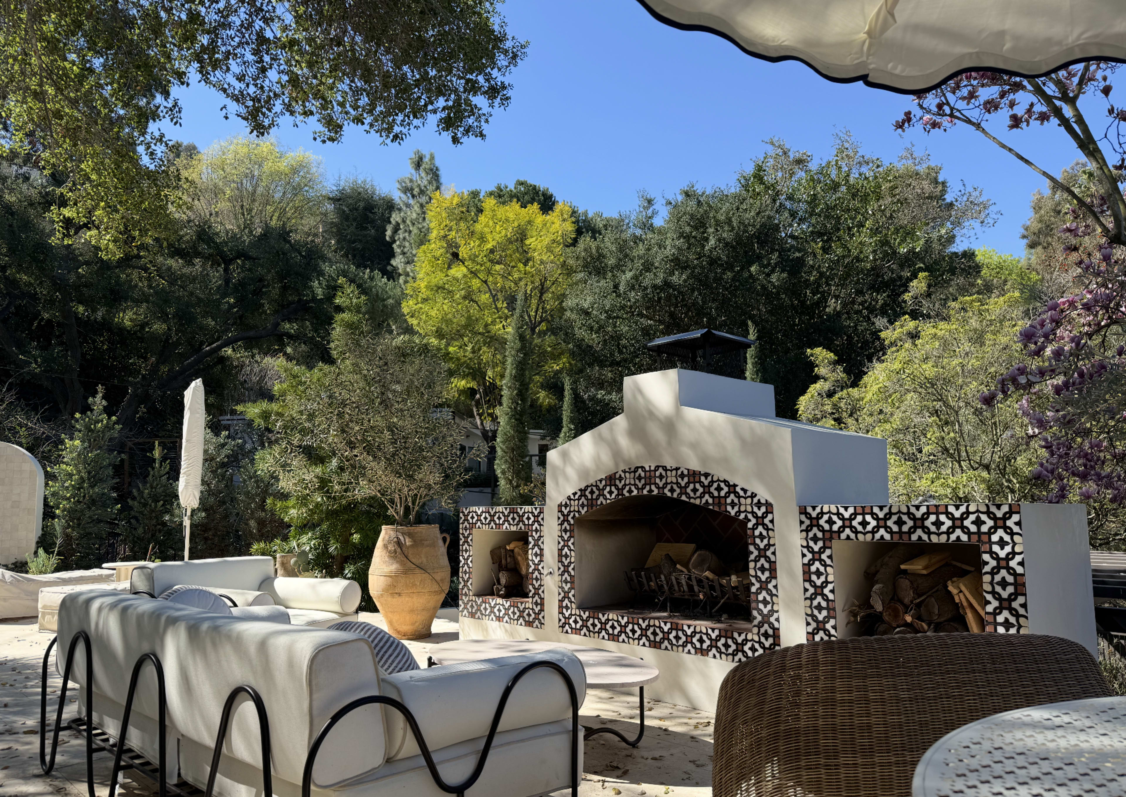 A patio area features a large outdoor fireplace adorned with decorative tiles, surrounded by comfortable seating and greenery.