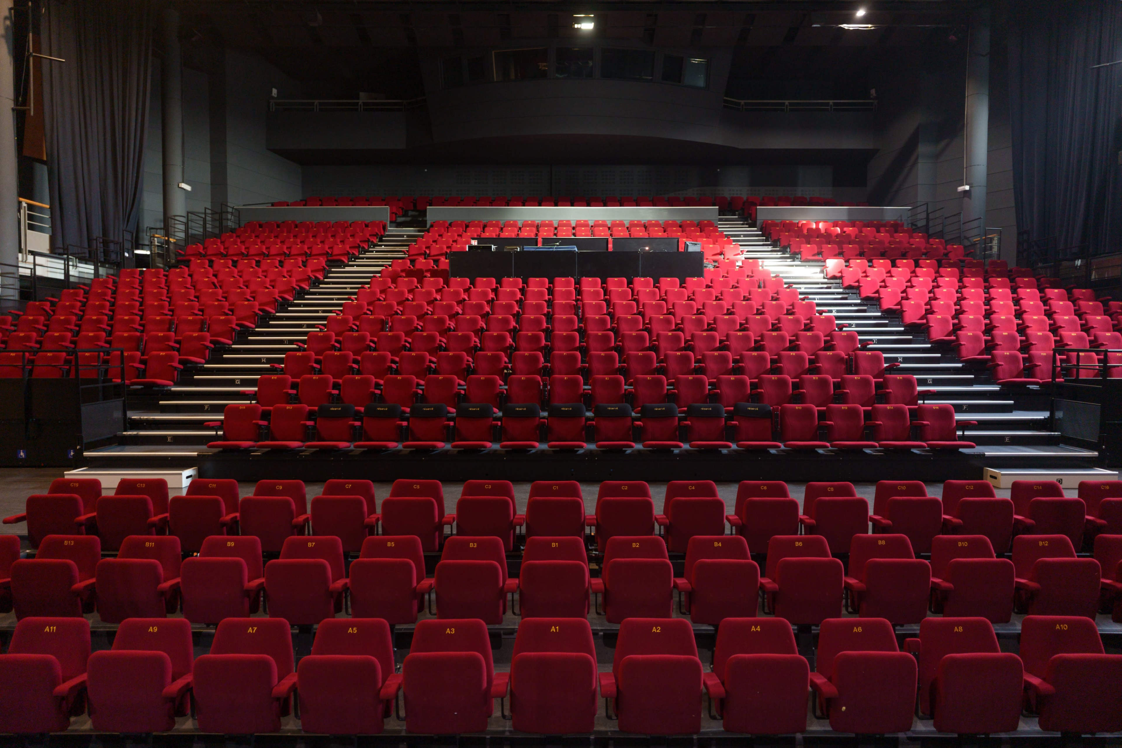 A large theater with numerous red seats arranged in rows on ascending levels.