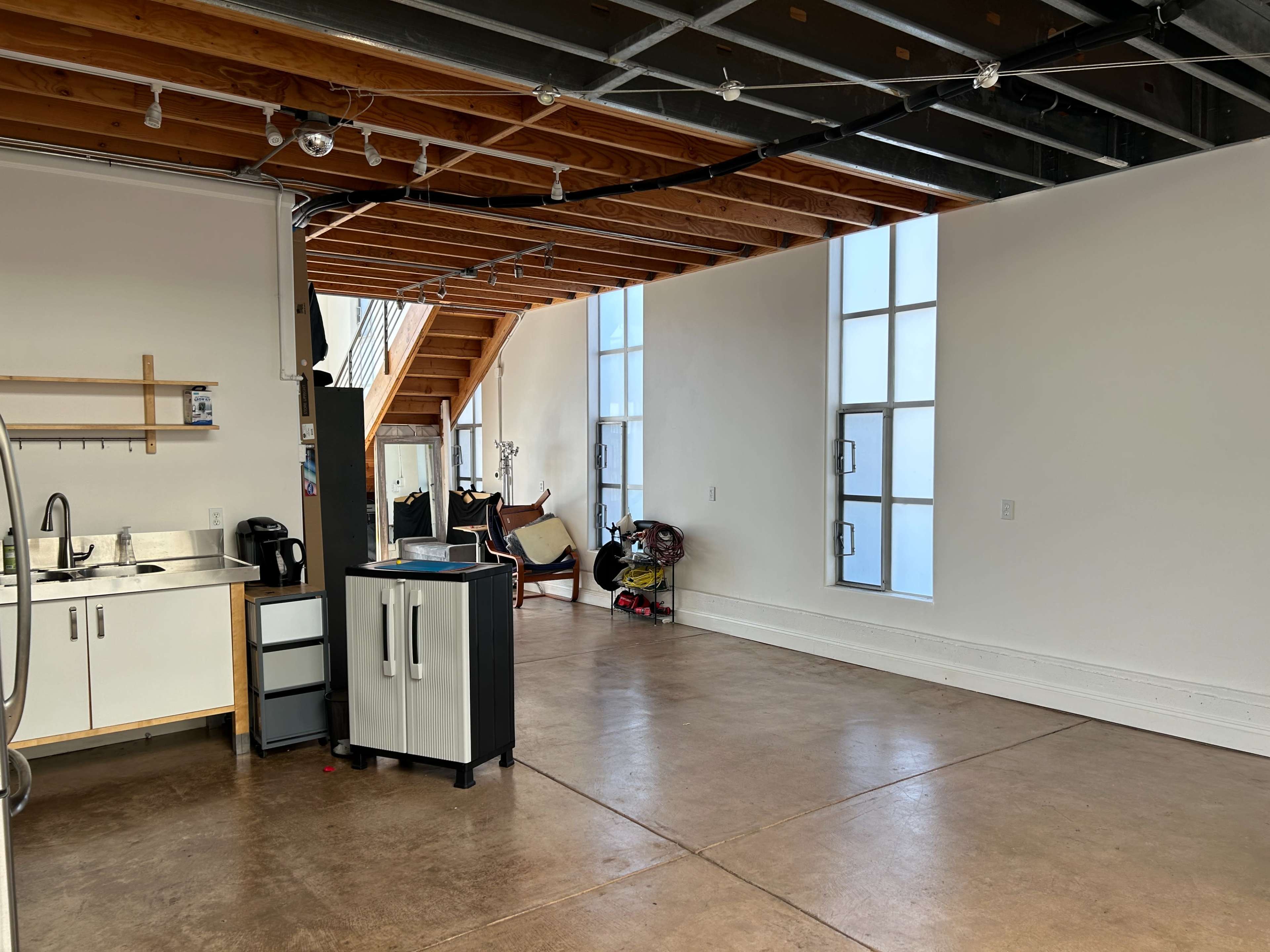 A spacious, unfinished room with exposed wooden beams, large windows, and a staircase in the background.