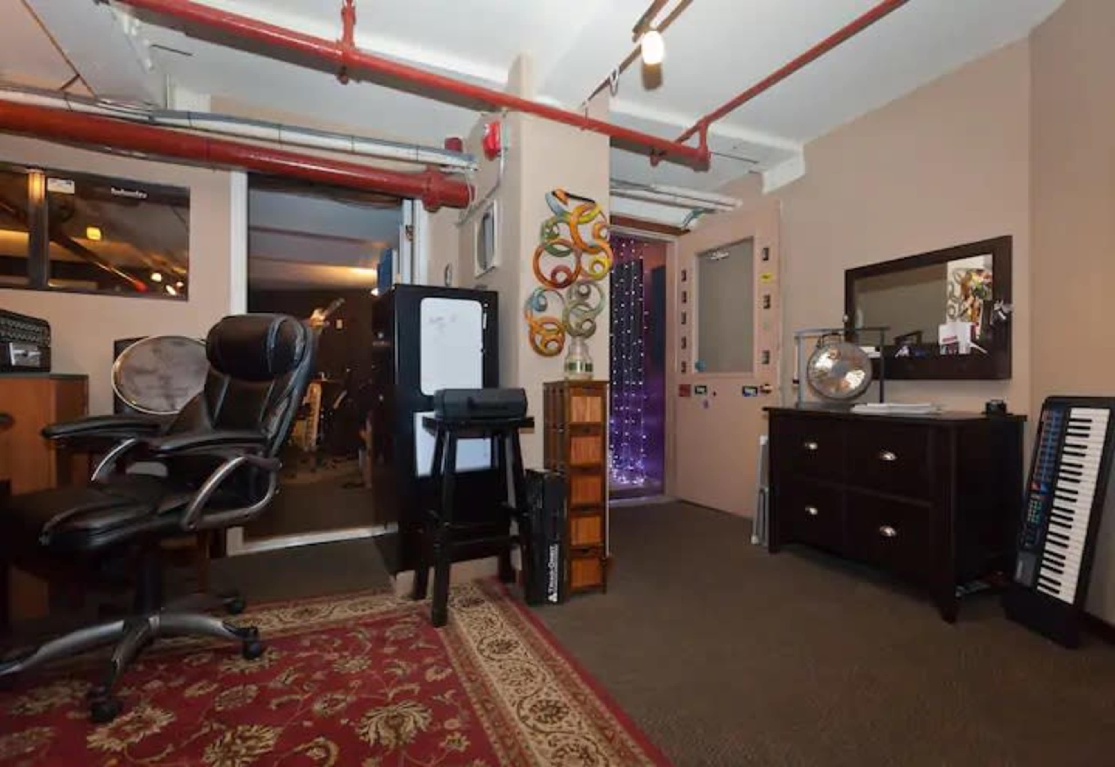 An office space with two black chairs, a wooden cabinet, and various items on the walls, including decorative pieces and a standing keyboard.
