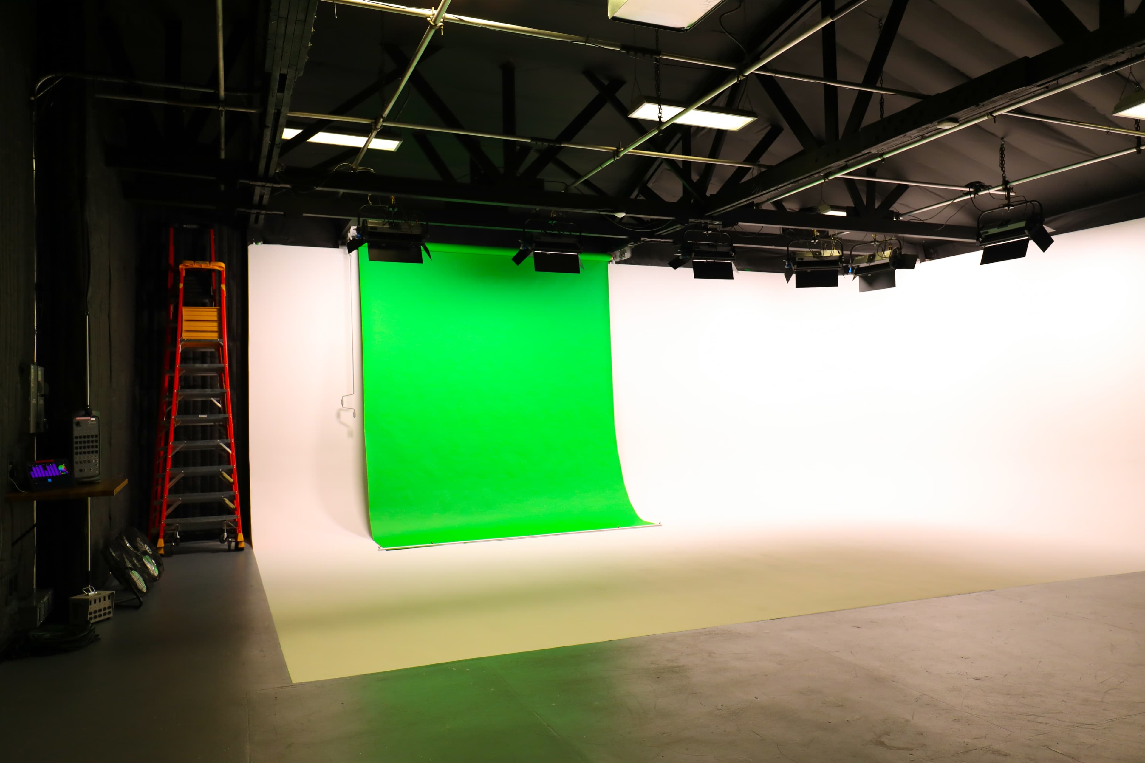 The image shows a photo studio with a green screen backdrop, white walls, and studio lighting.