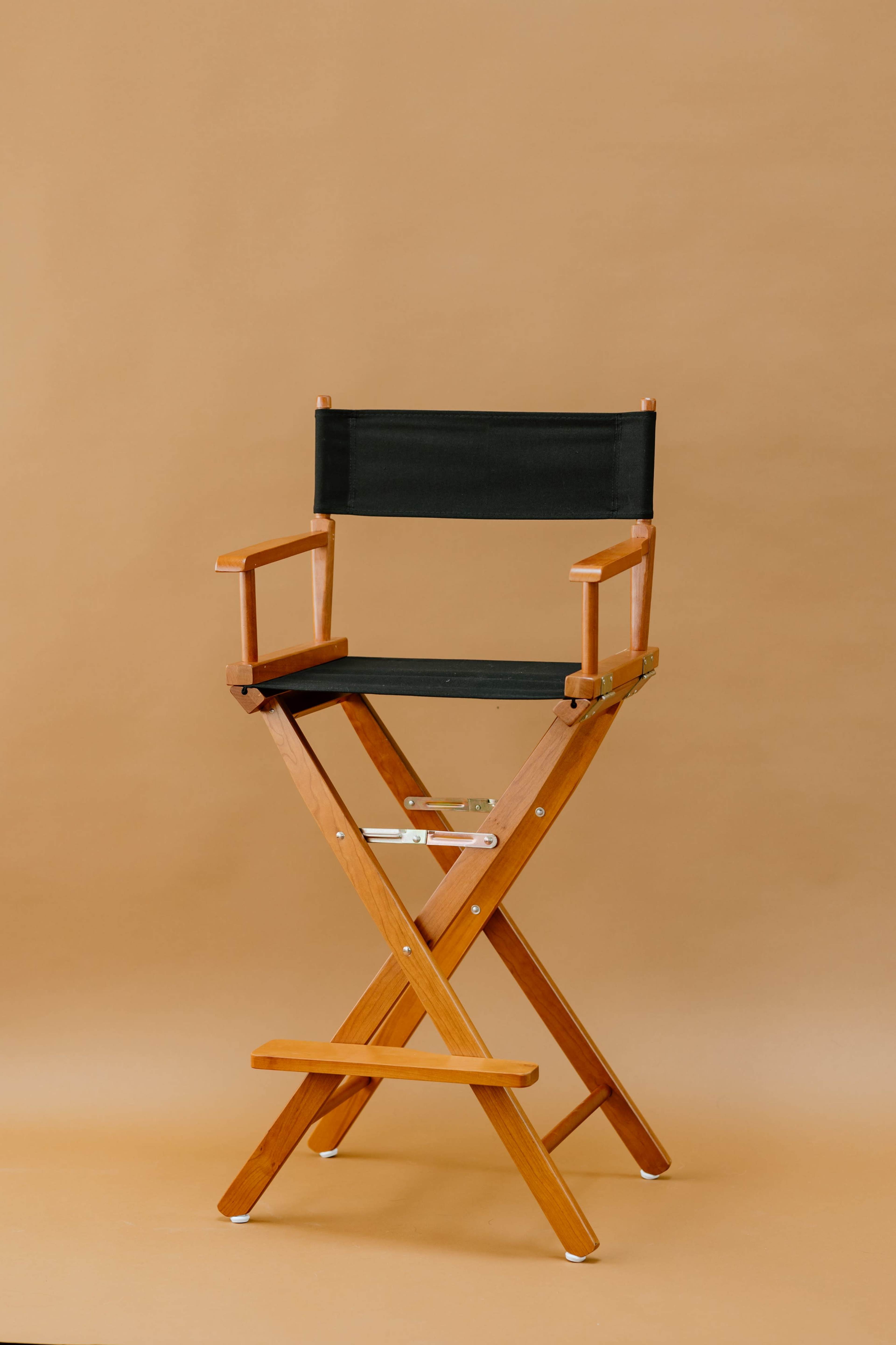 A wooden director's chair with a dark green canvas seat and backrest is positioned against a beige backdrop.