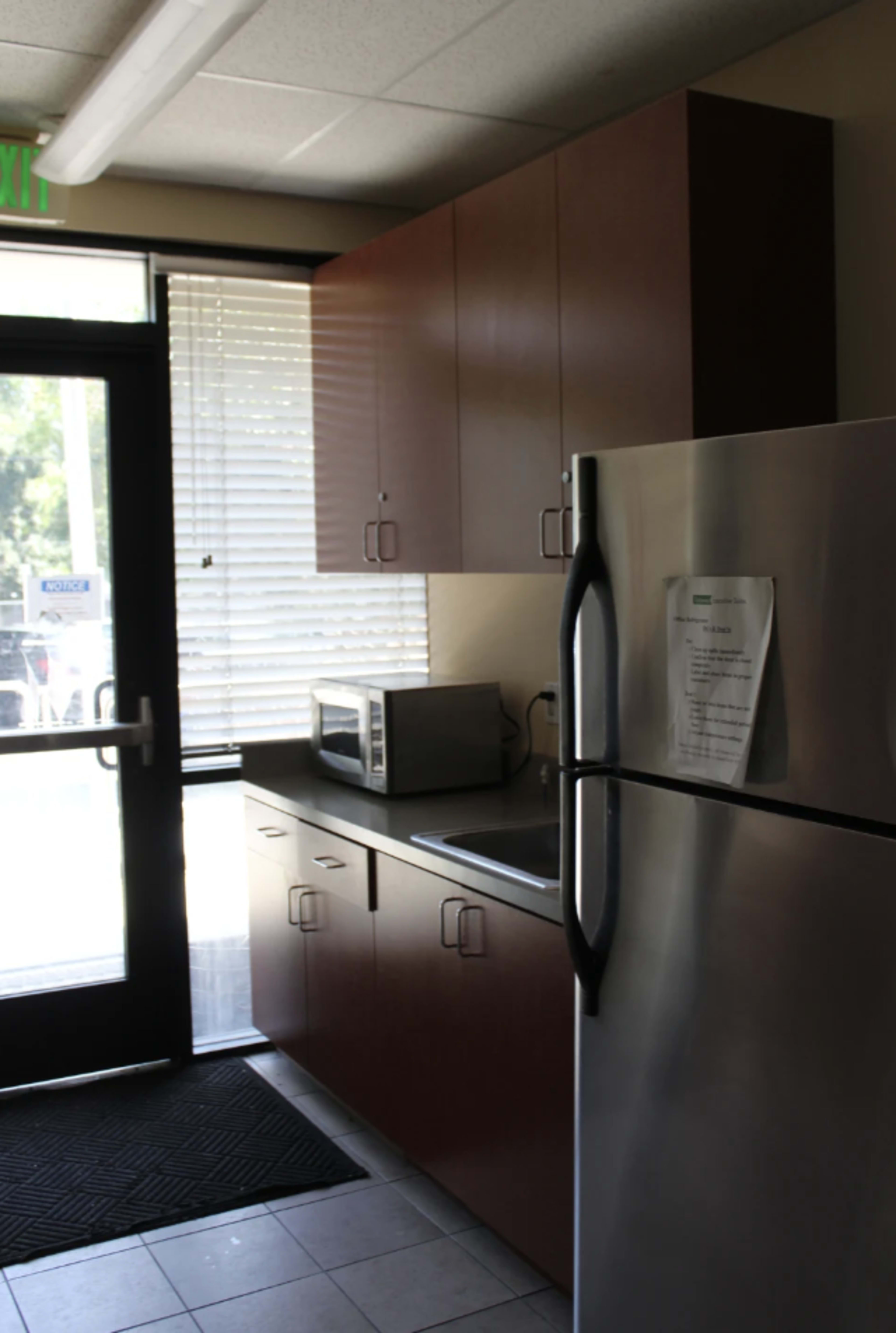 A kitchen area with wooden cabinets, a stainless steel refrigerator, a microwave, and a doorway leading outside.