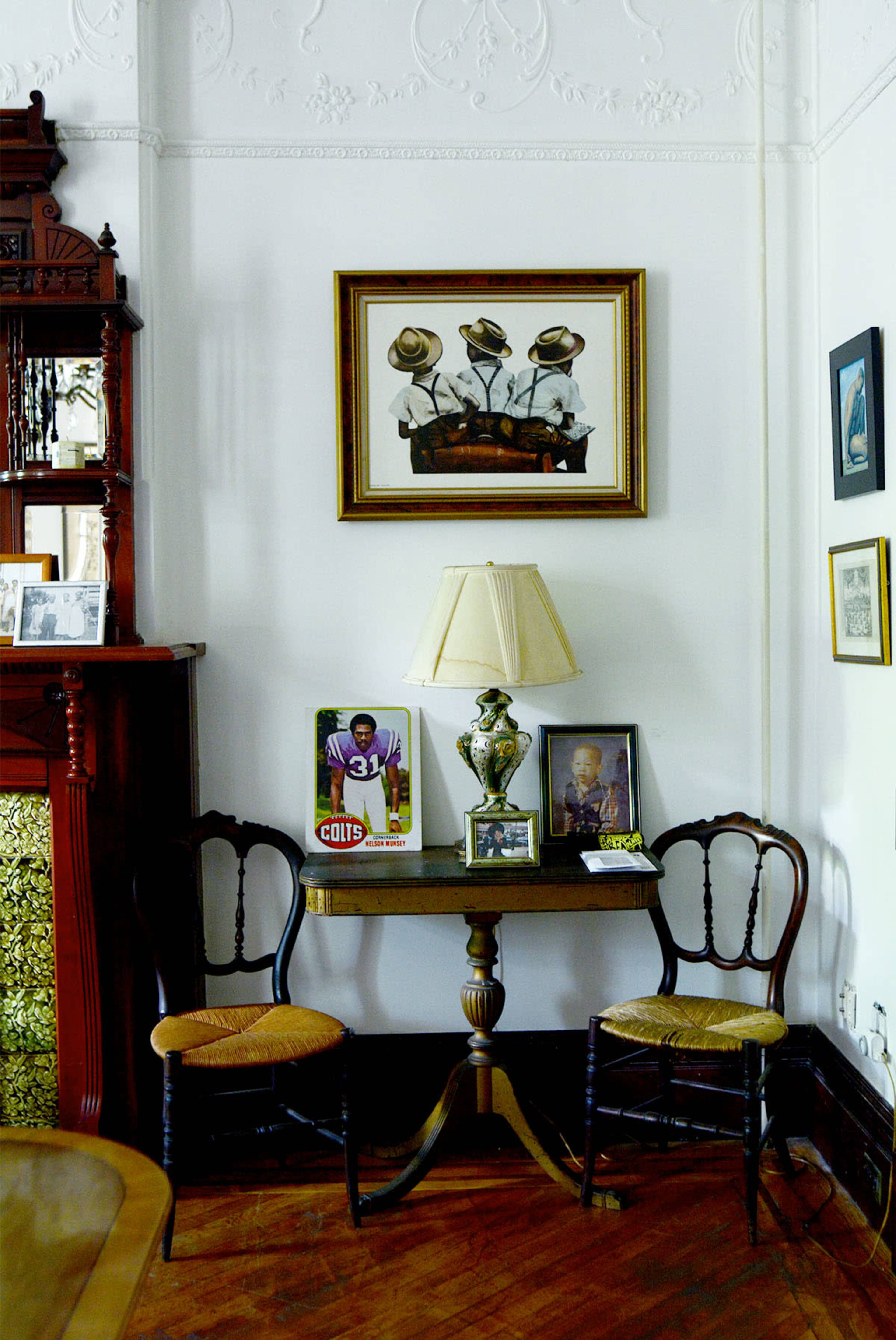 A small table with two chairs is positioned in a corner of a room adorned with framed pictures and a lamp.