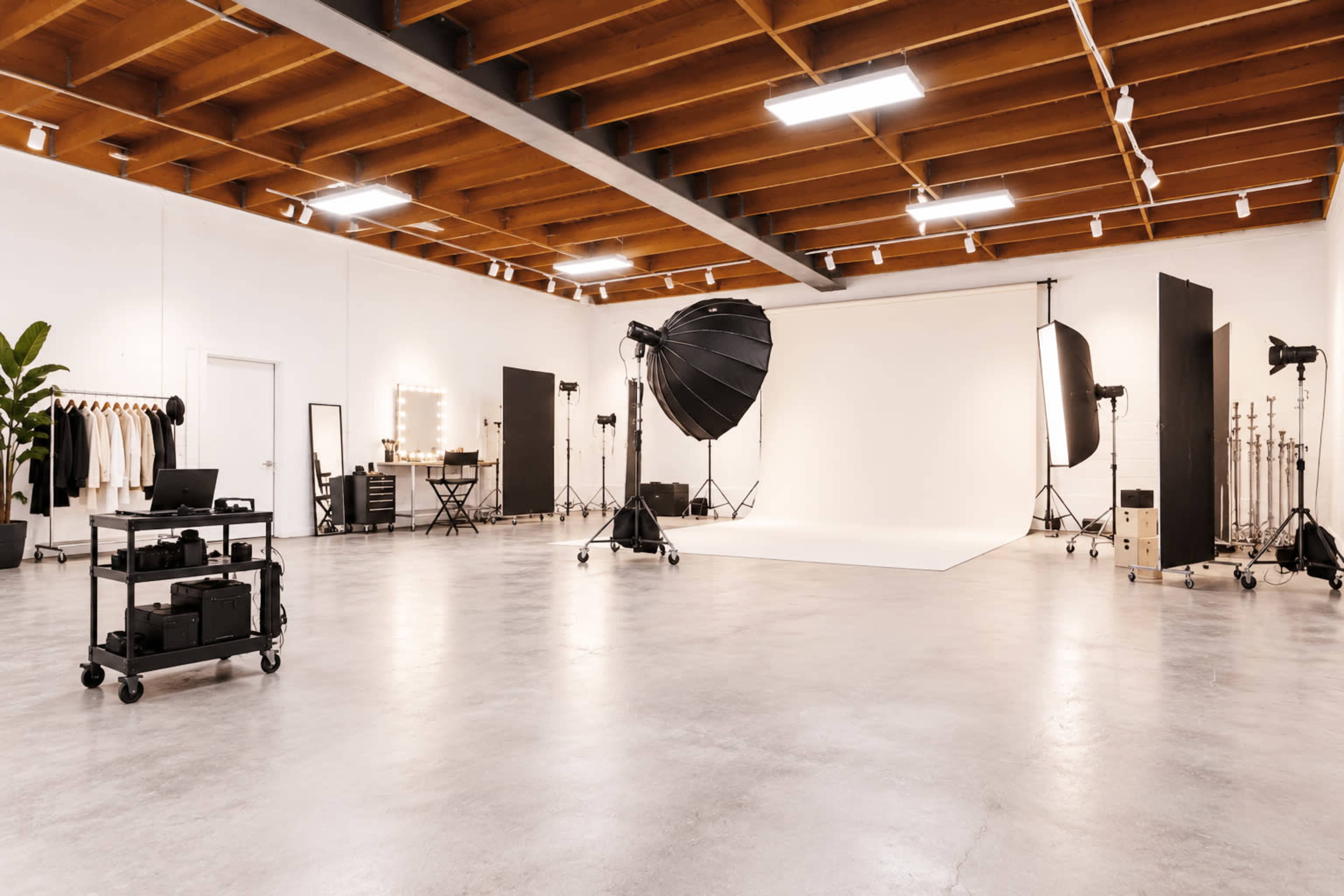 The image shows a spacious photography studio with a backdrop, lighting equipment, and a variety of props and furniture arranged throughout the room.