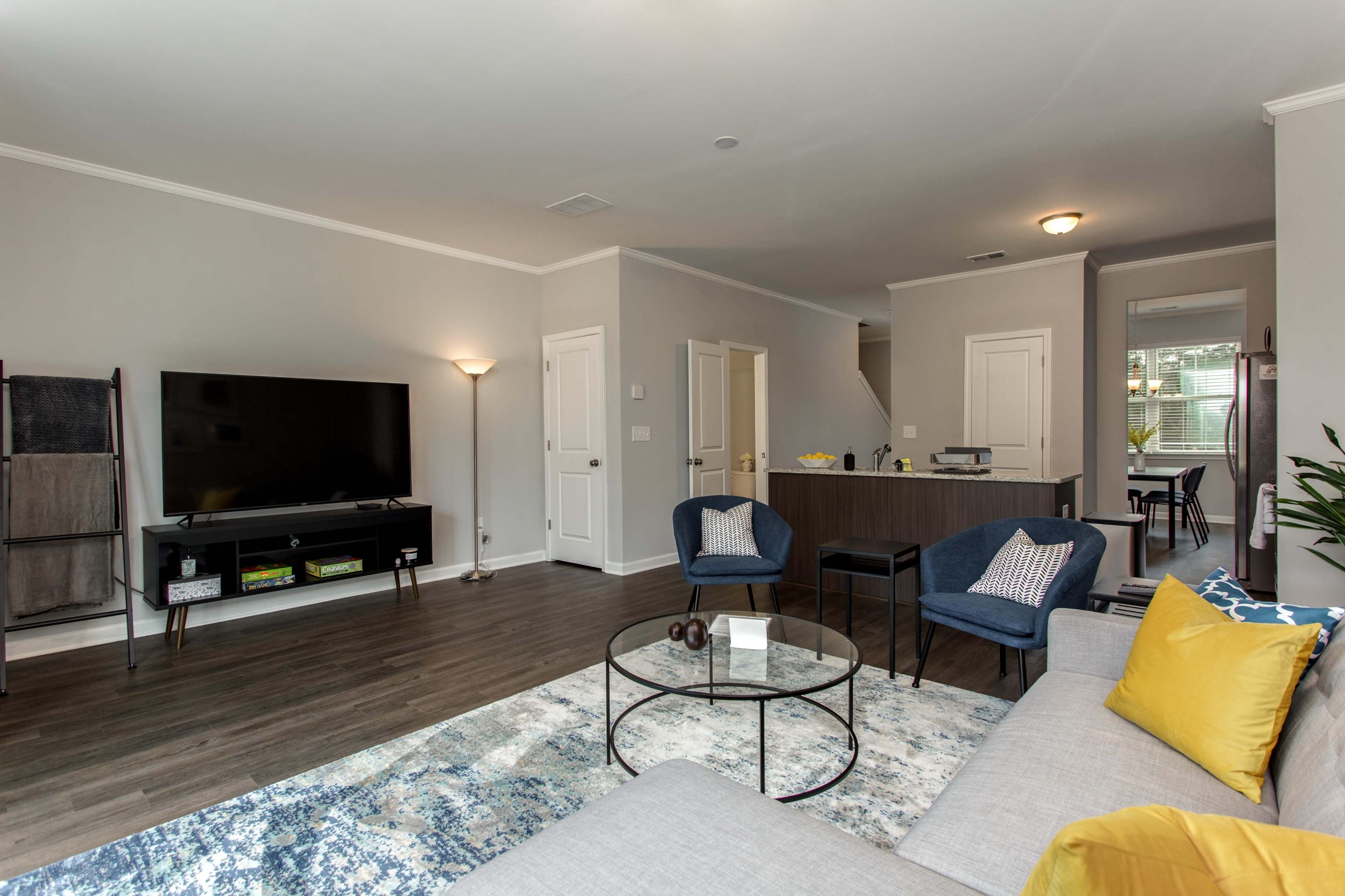 A modern living room with a sectional sofa, coffee table, television, and a dining area visible in the background.