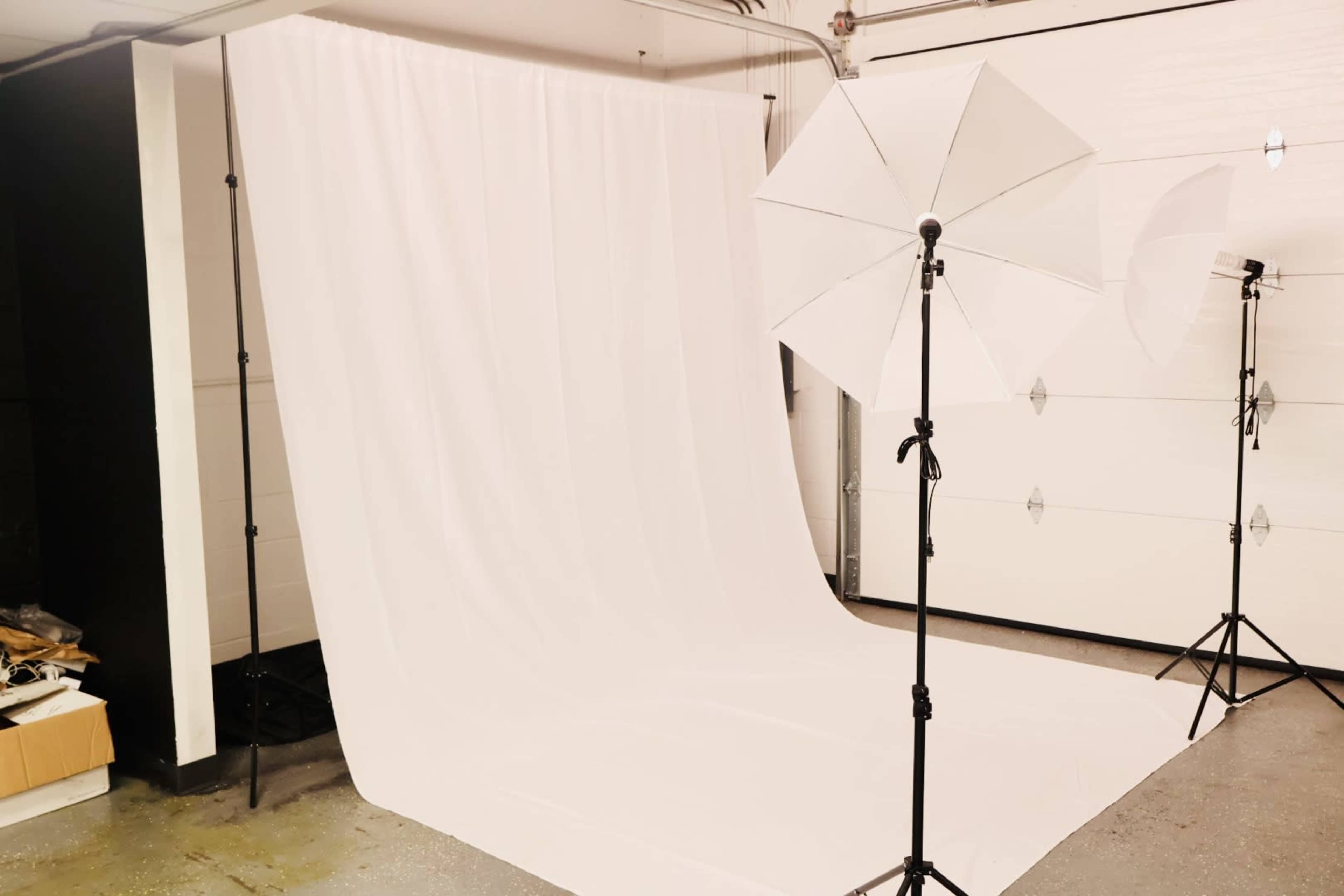 A photography studio setup with a white backdrop and lighting equipment arranged in a garage space.