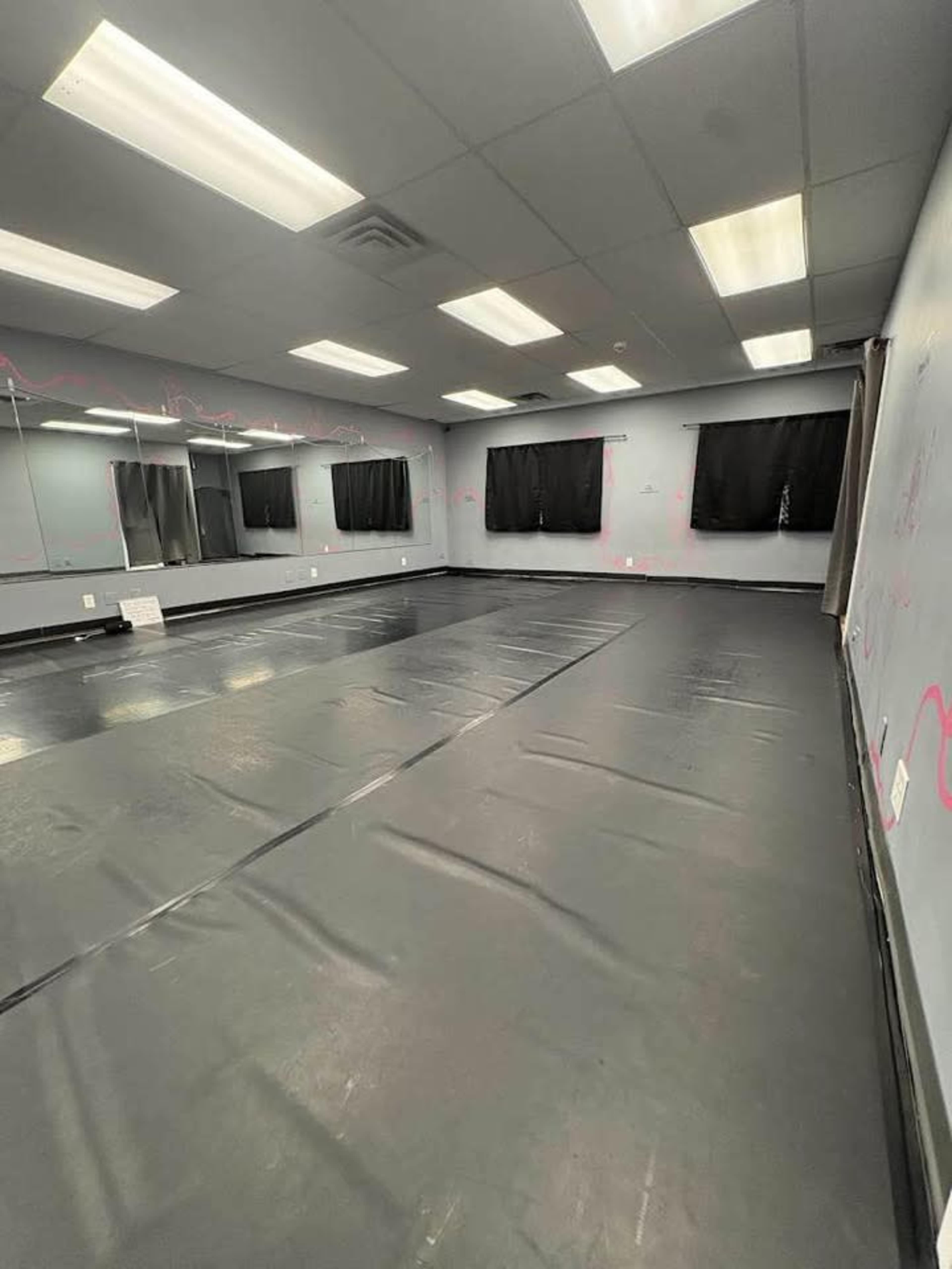 The image shows a spacious, empty room with a black floor, large mirrors on one wall, and dark curtains covering the windows.