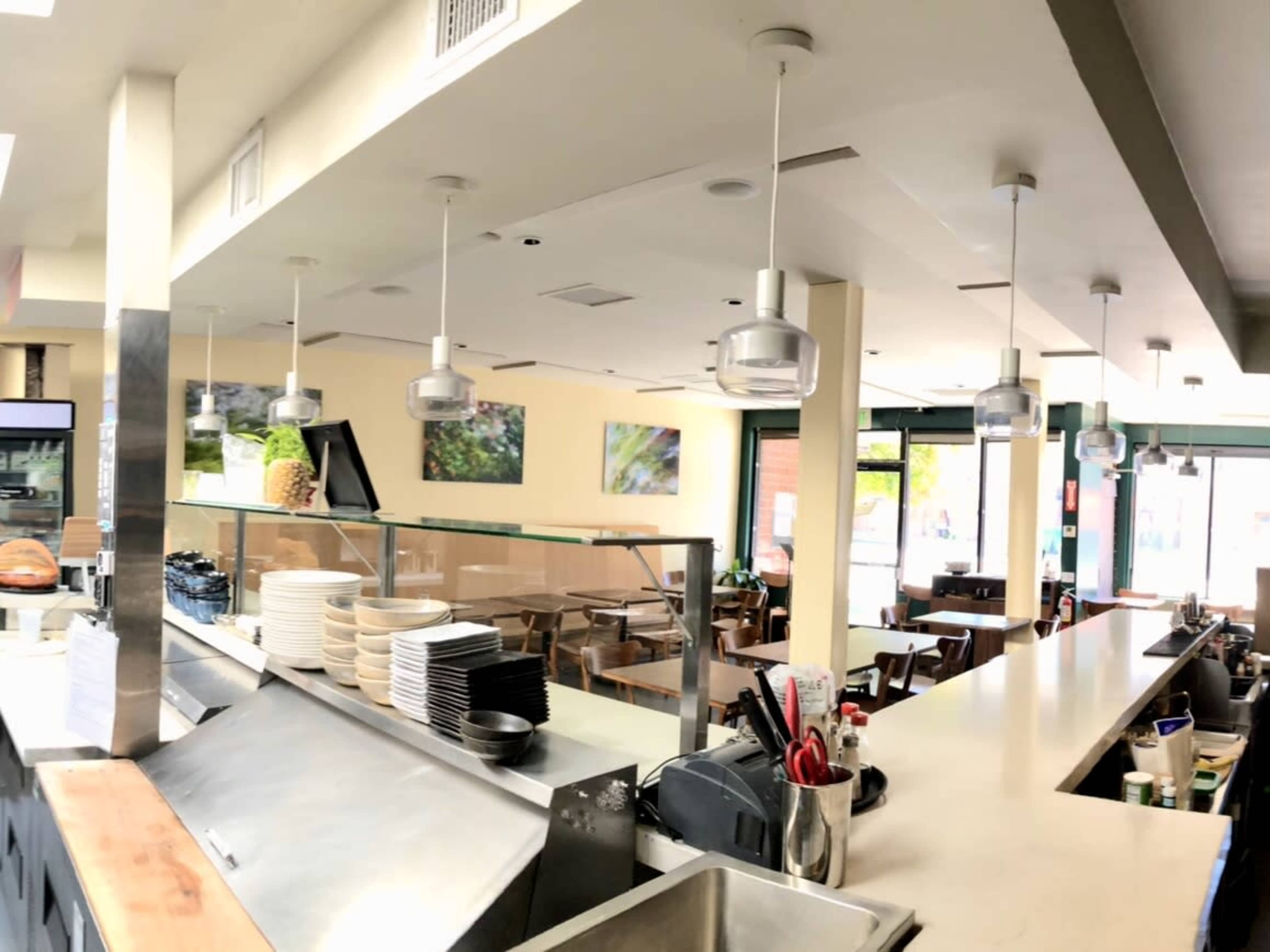 The interior of a café featuring a long counter, hanging light fixtures, and a dining area with tables and chairs.