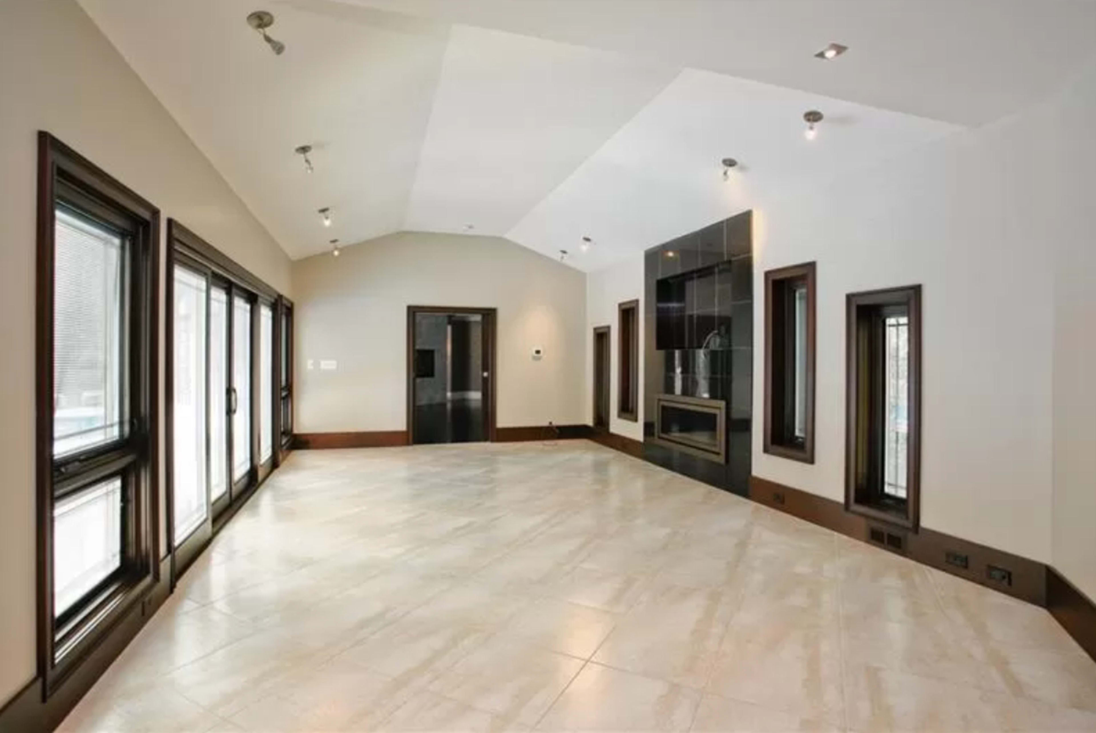 A spacious, well-lit room with large windows, tiled flooring, and a fireplace.
