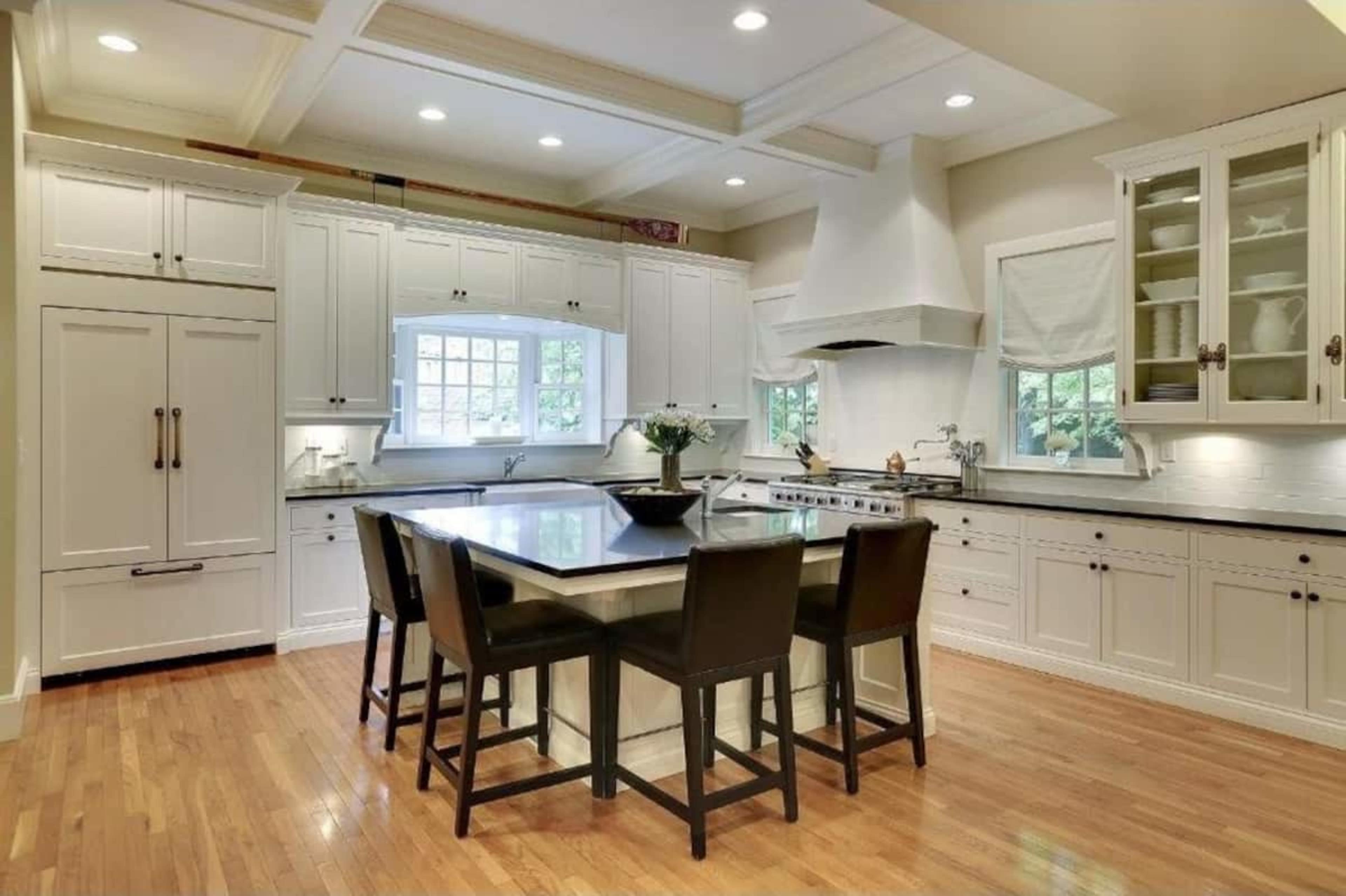 A modern kitchen features white cabinetry, a central island with seating, and hardwood flooring.