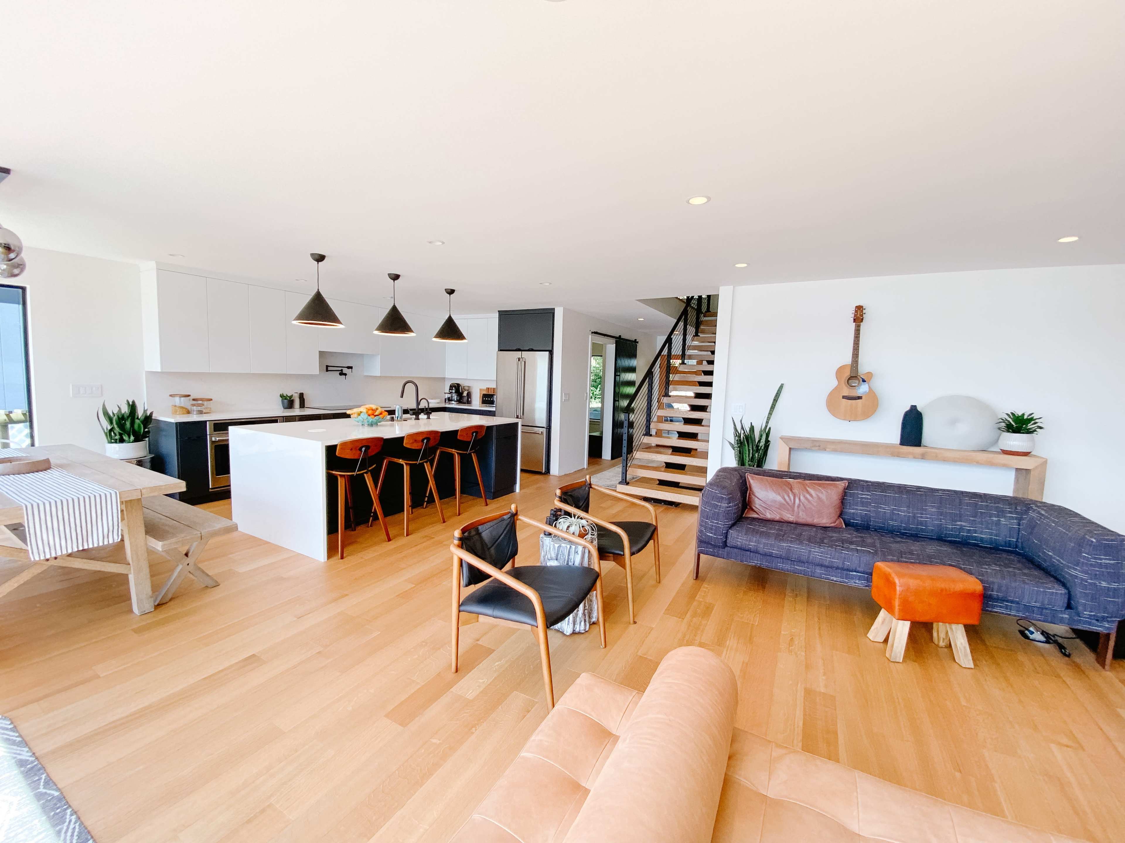A modern open-concept living space featuring a kitchen with black cabinetry, a dining area with a wooden table, and a cozy seating area with various chairs and sofas.