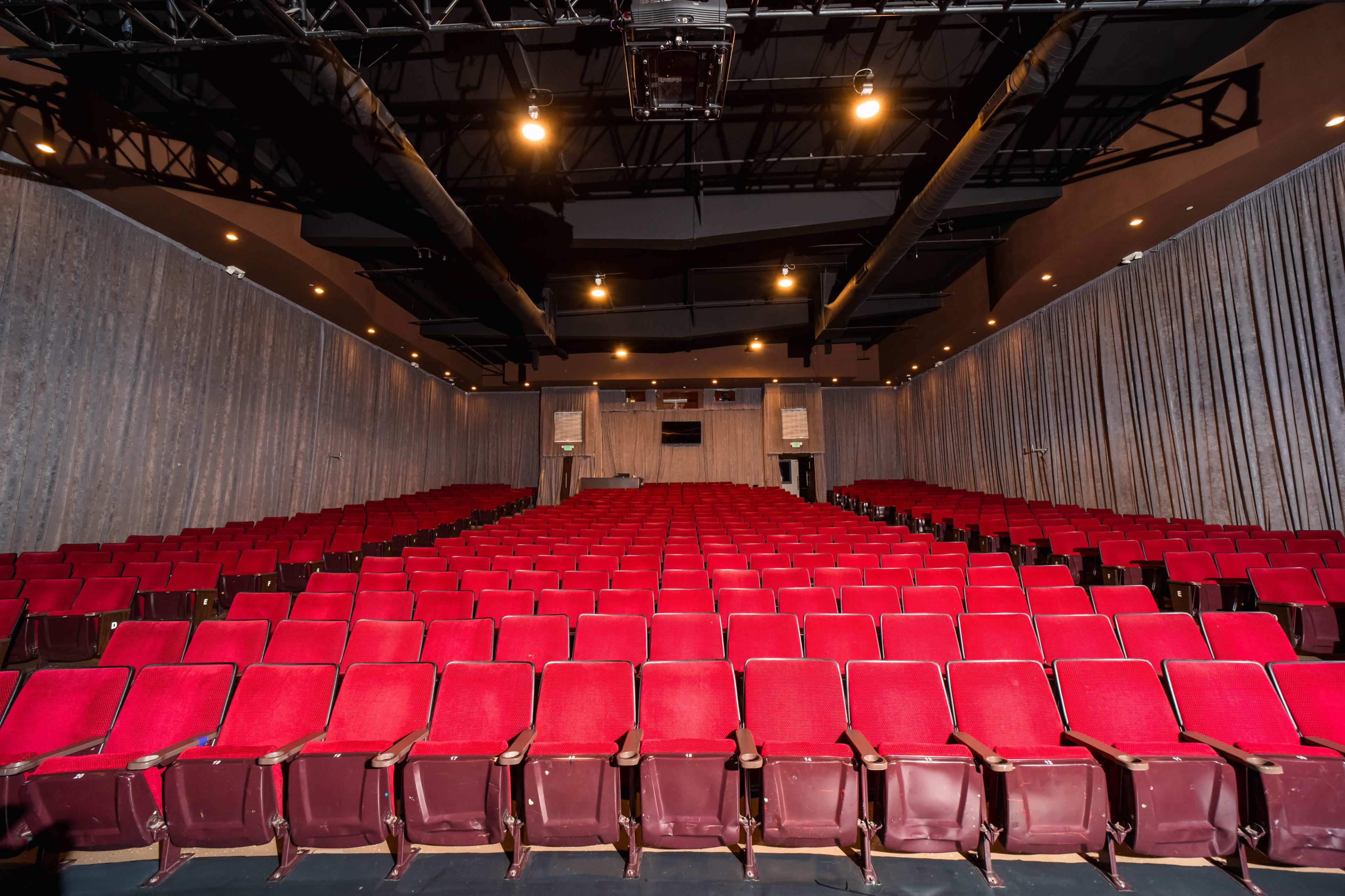A nearly empty theater features rows of red seats arranged in a symmetrical layout under dim lighting.