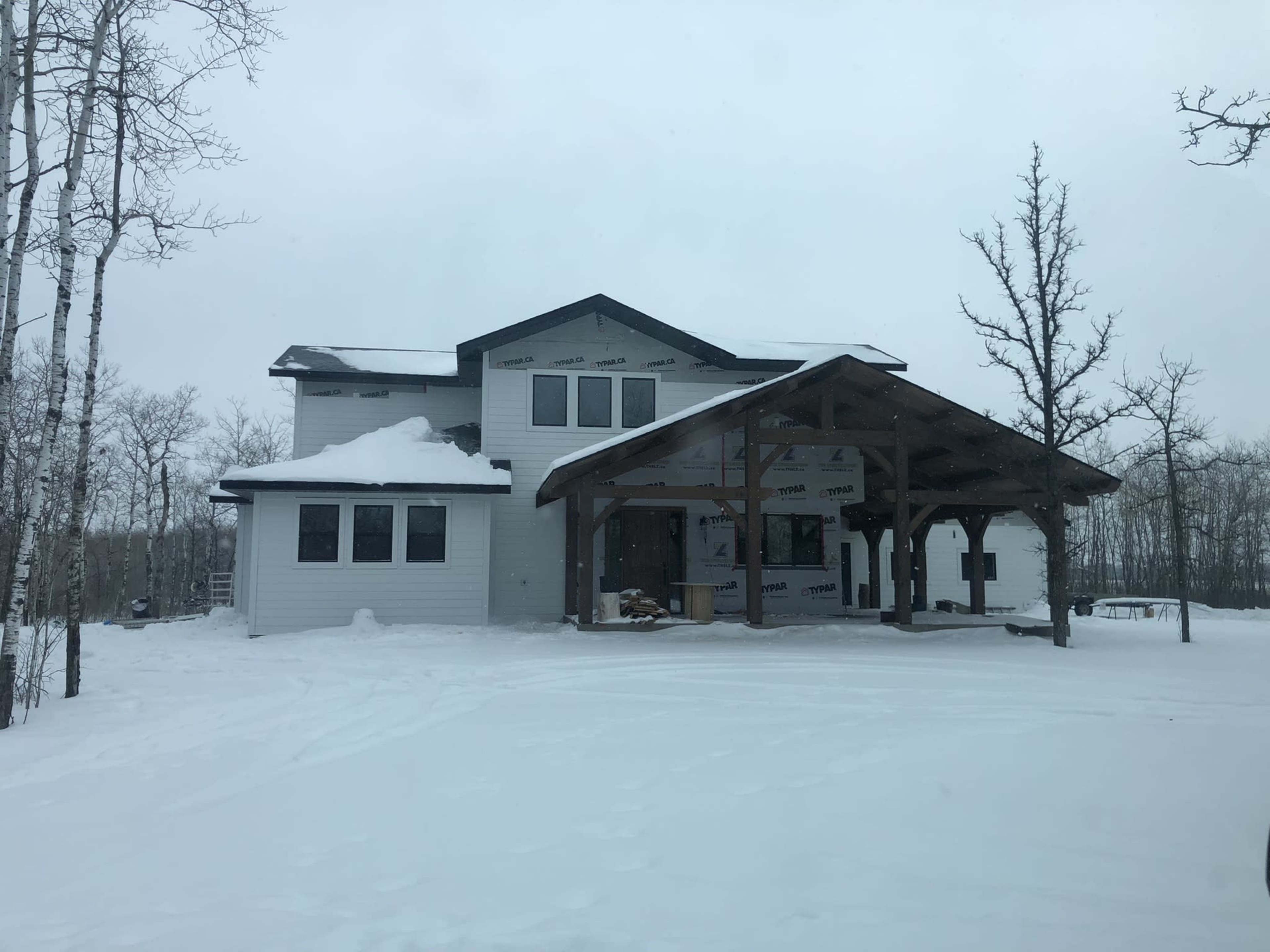 A partially constructed house in a snowy landscape with bare trees surrounding it.