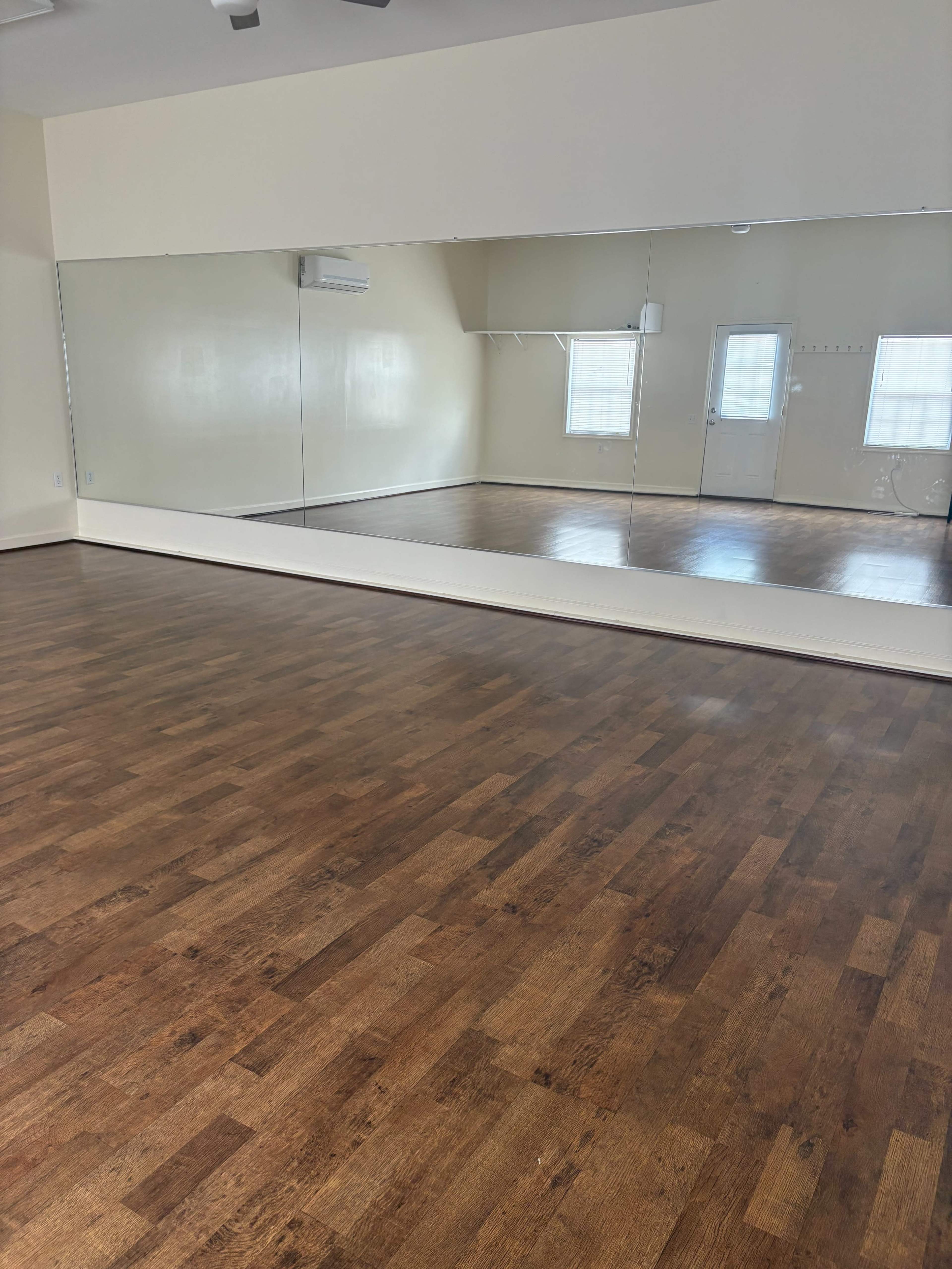 The image shows a spacious room with a polished wooden floor and a large mirror along one wall.