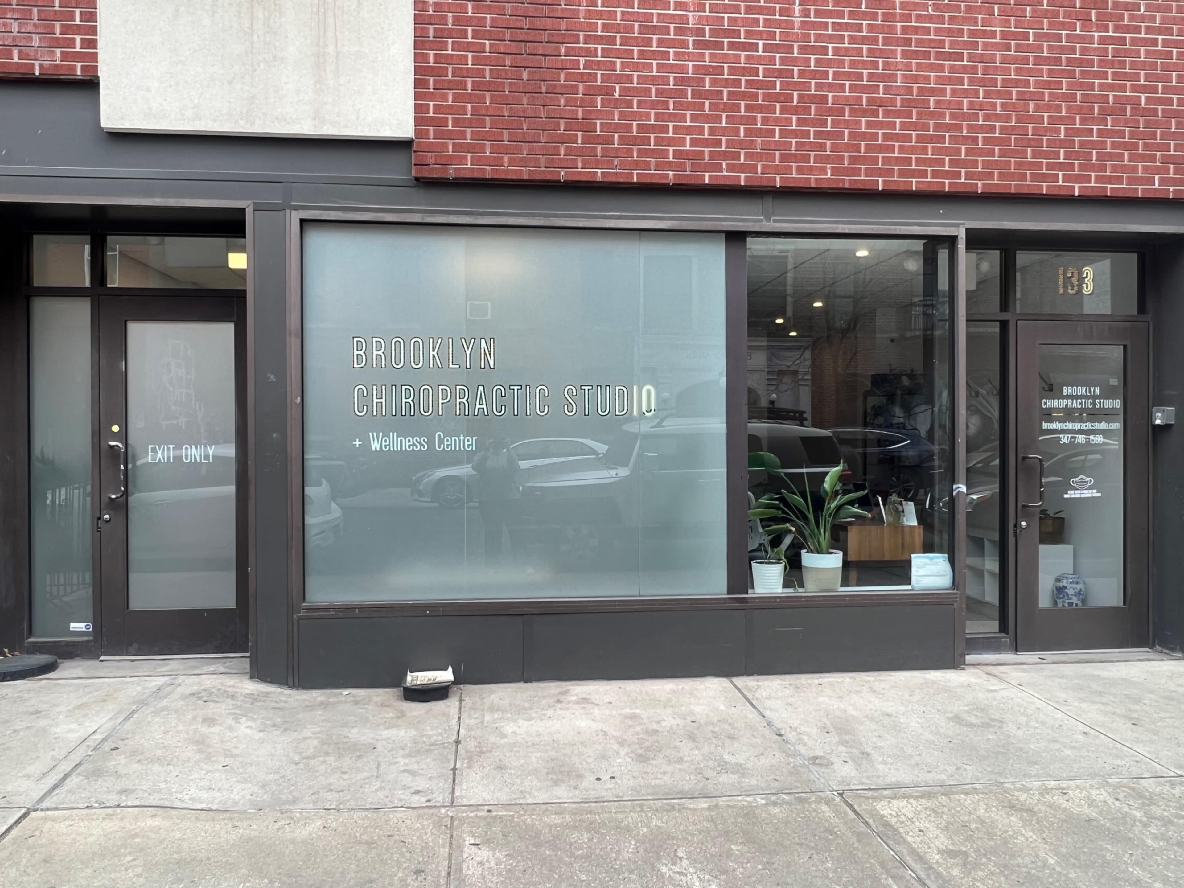 The image shows a storefront labeled "Brooklyn Chiropractic Studio + Wellness Center" with large glass windows and a modern aesthetic.