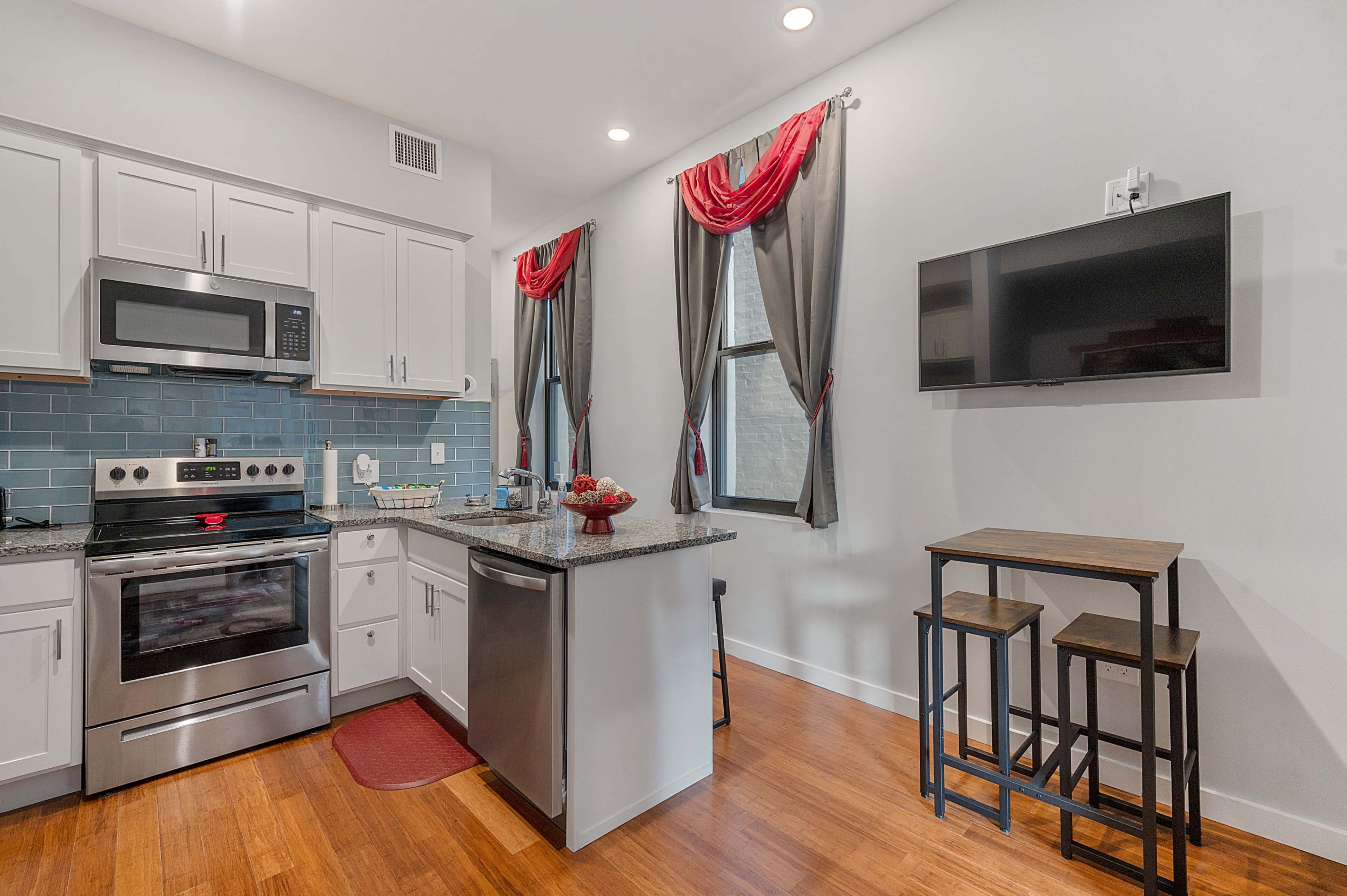 A modern kitchen with stainless steel appliances, white cabinetry, and a small dining area featuring a table with two stools.