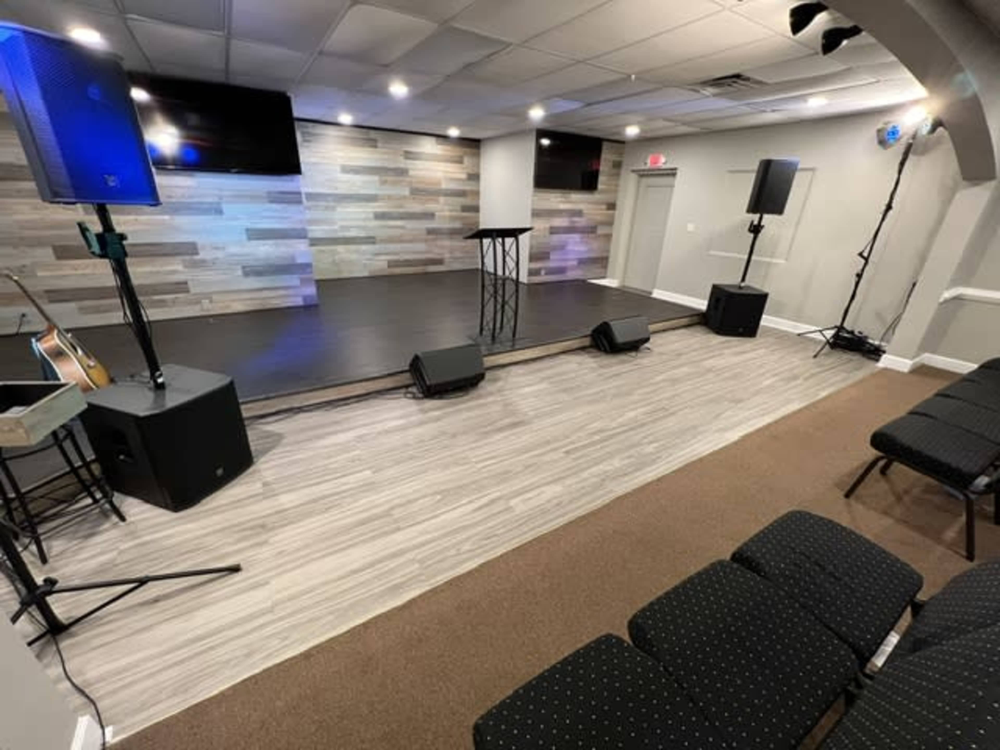 A small stage area with a podium, amplifiers, and a seating arrangement in a well-lit indoor space.