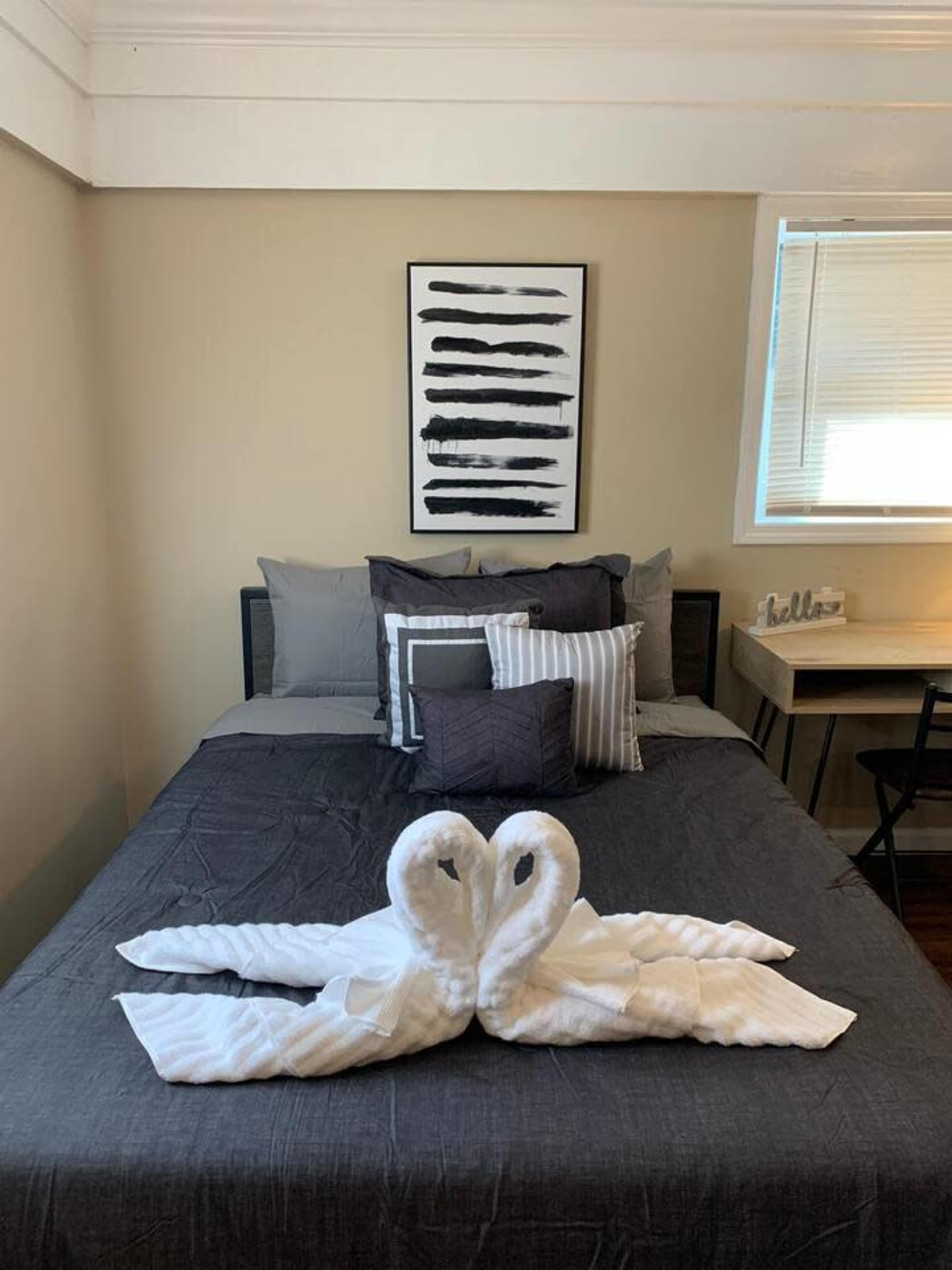 A neatly made bed with gray linens features two towel swans at the foot and decorative pillows arranged on top.