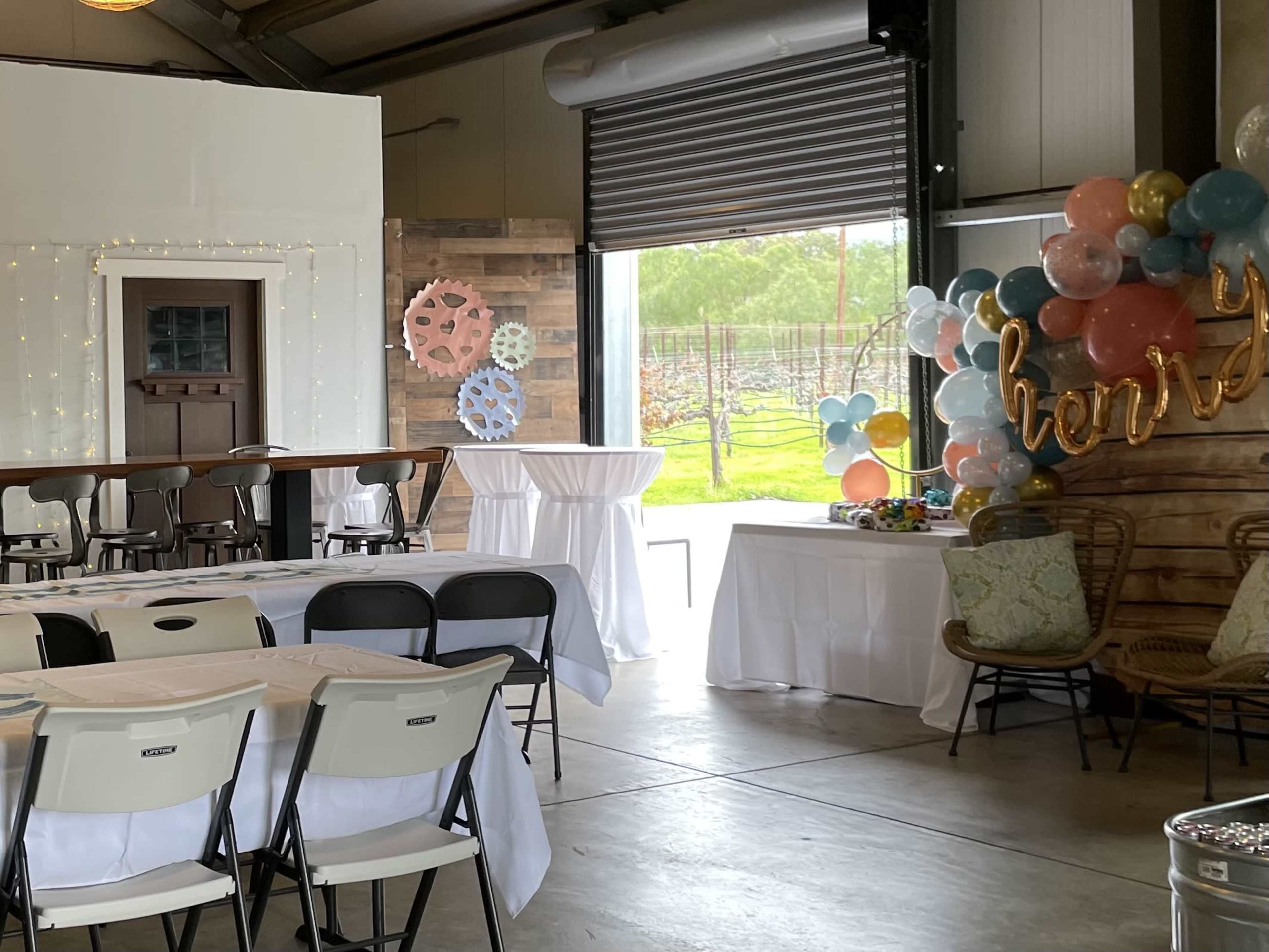 The image shows an event space with decorated tables, a balloon arch, and large gears displayed on the walls.