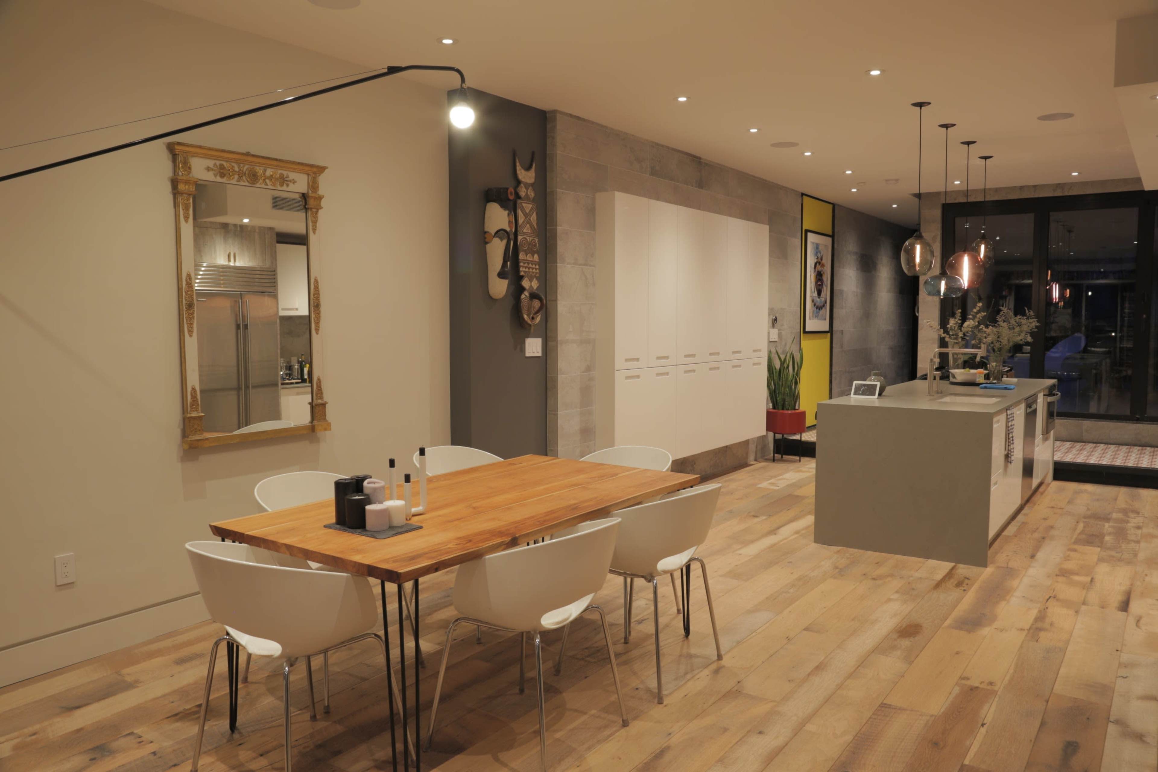 A spacious modern kitchen and dining area features a wooden dining table with white chairs, a large island counter, and decorative elements on the walls.