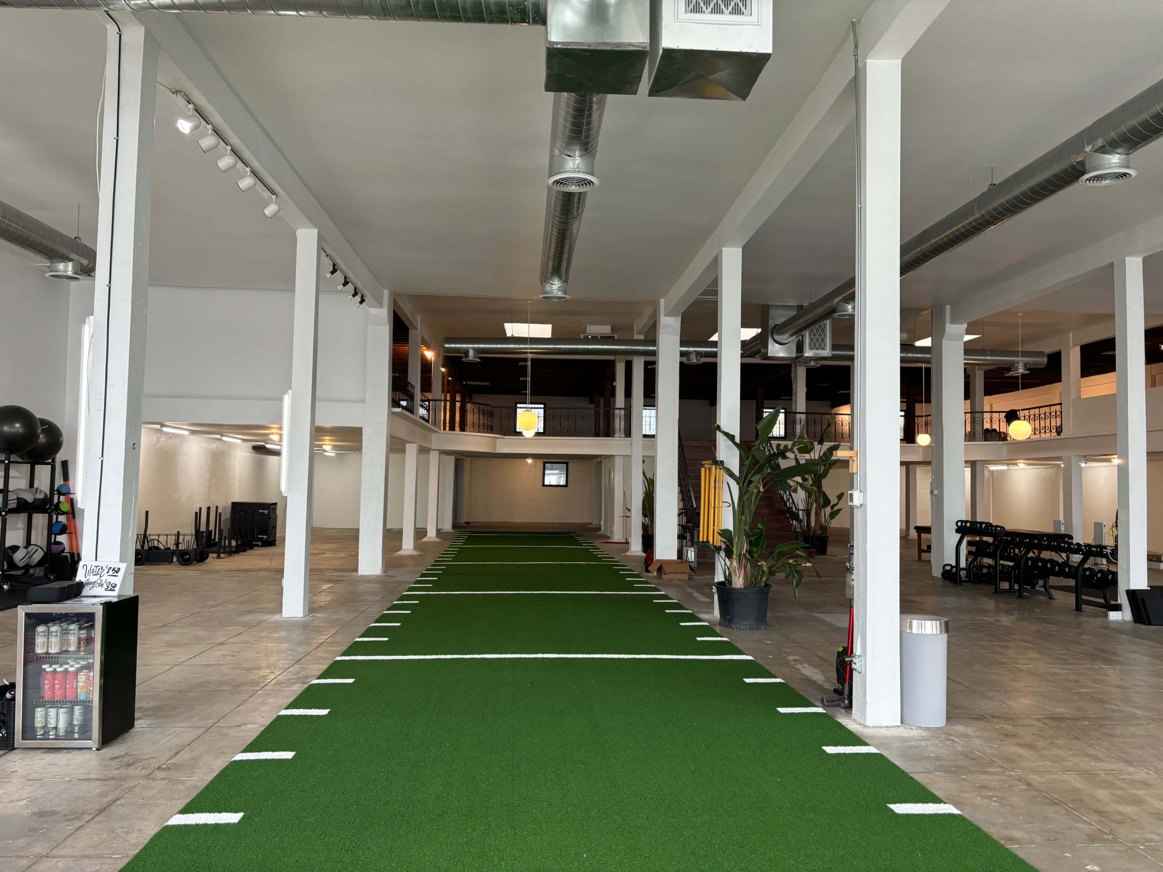 A spacious indoor gym with artificial turf running lanes and various workout equipment arranged along the sides.